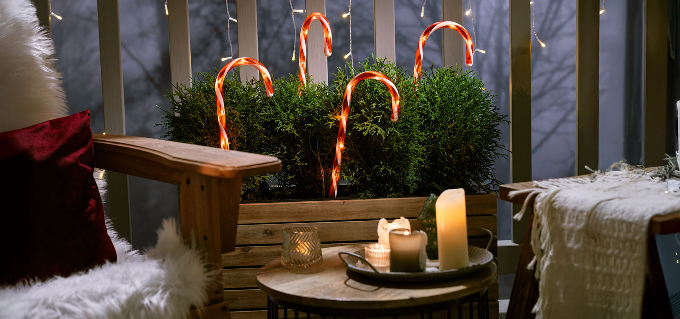 Коледно декориран балкон със стол, свещи и бонбонени бастунчета.