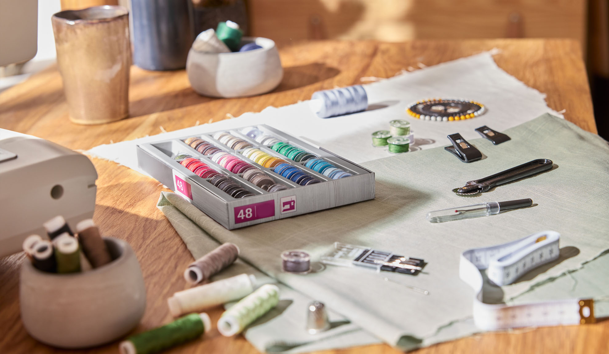 Шивашки комплект с кутия цветни конци, шевна машина и различни инструменти на дървена маса.