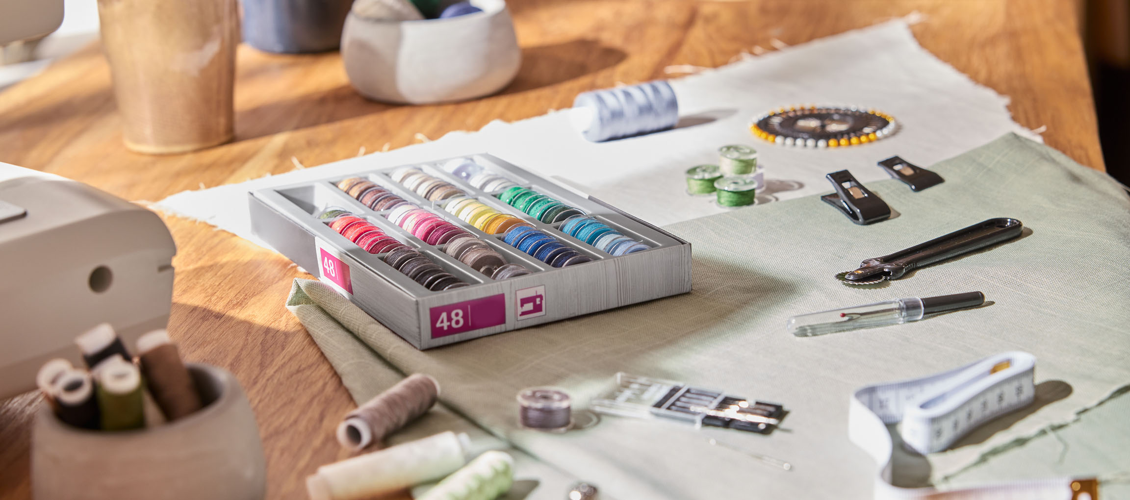 Шевни принадлежности на дървена маса, включително органайзер за конци с 48 макари, плат и различни инструменти.