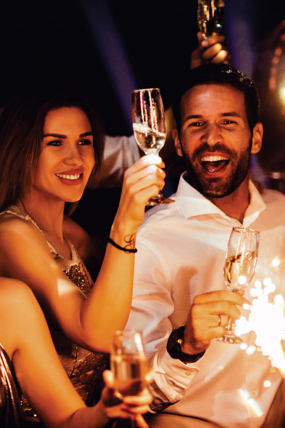 Мъж и жена празнуват с чаши шампанско и бенгалски огън.