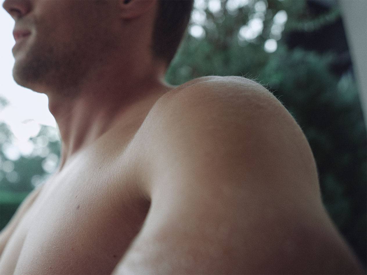 Близък план на мъжко рамо и врат, с размазан зелен фон.