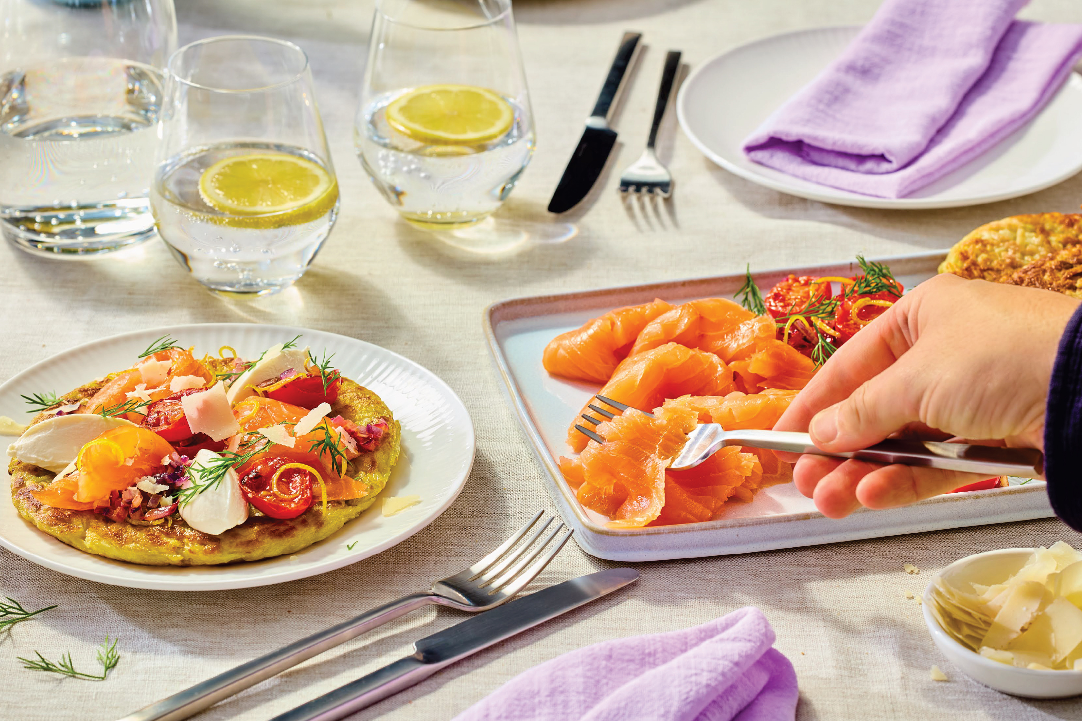 Панкейк със сьомга, домати и сирене, сервиран с вода с лимон и прибори.