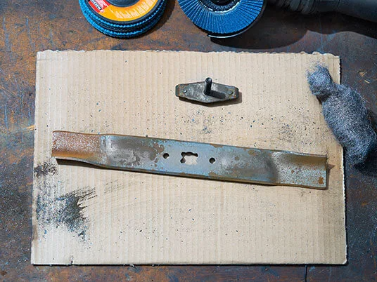 Ръждясало острие на косачка върху картон с абразивни дискове и стоманена вълна.