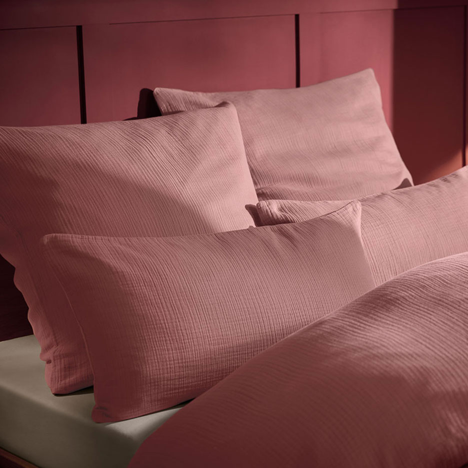 Розова муселинова възглавница и спално бельо на легло с дървена табла.