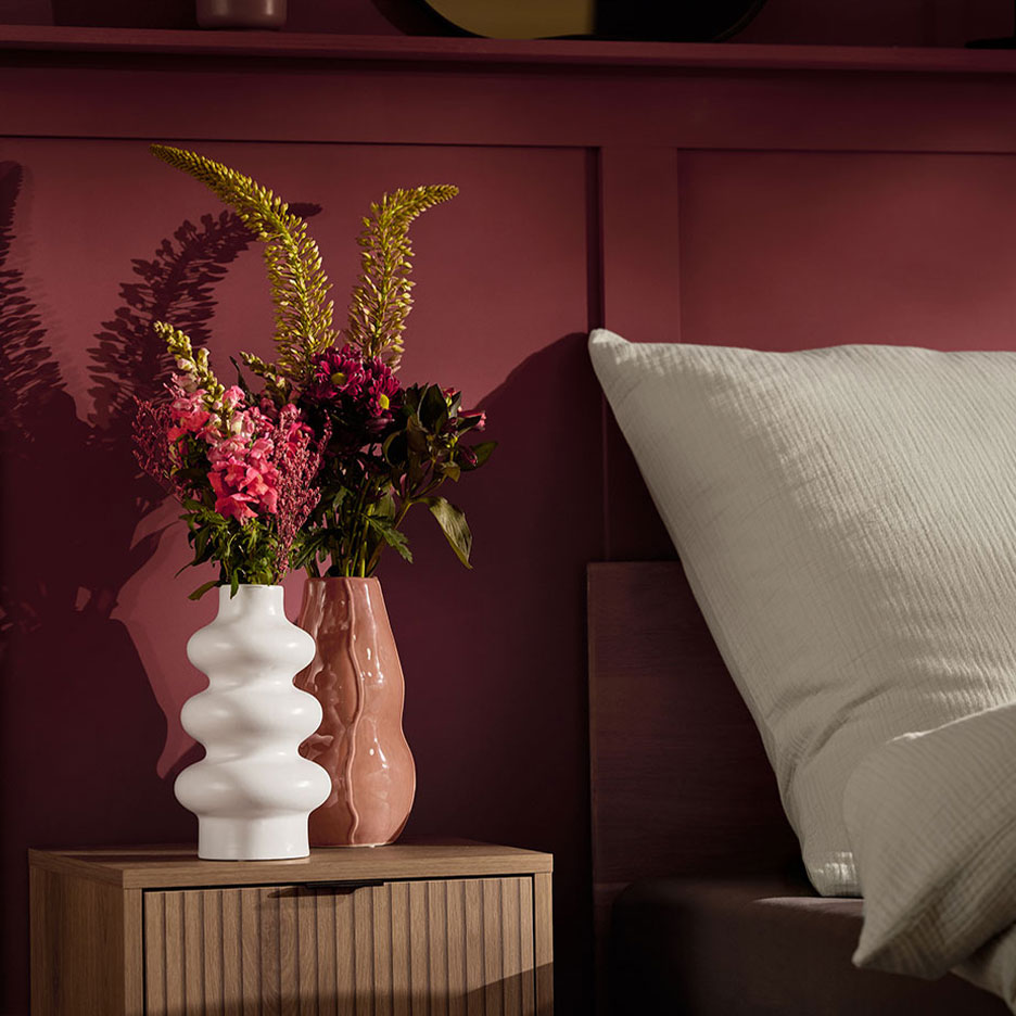 Две вази с цветя на нощно шкафче до легло с бяла възглавница.