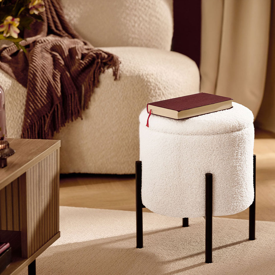 Бяла пухкава табуретка с черни крака, червена книга, фотьойл и кафяво одеяло.