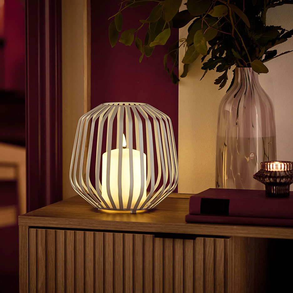 LED свещ в бял метален държач върху дървен скрин.