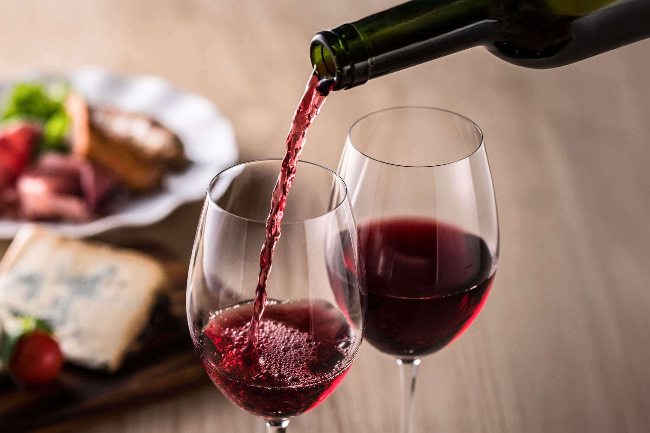 Червено вино се налива в чаша, с предястия на заден план.