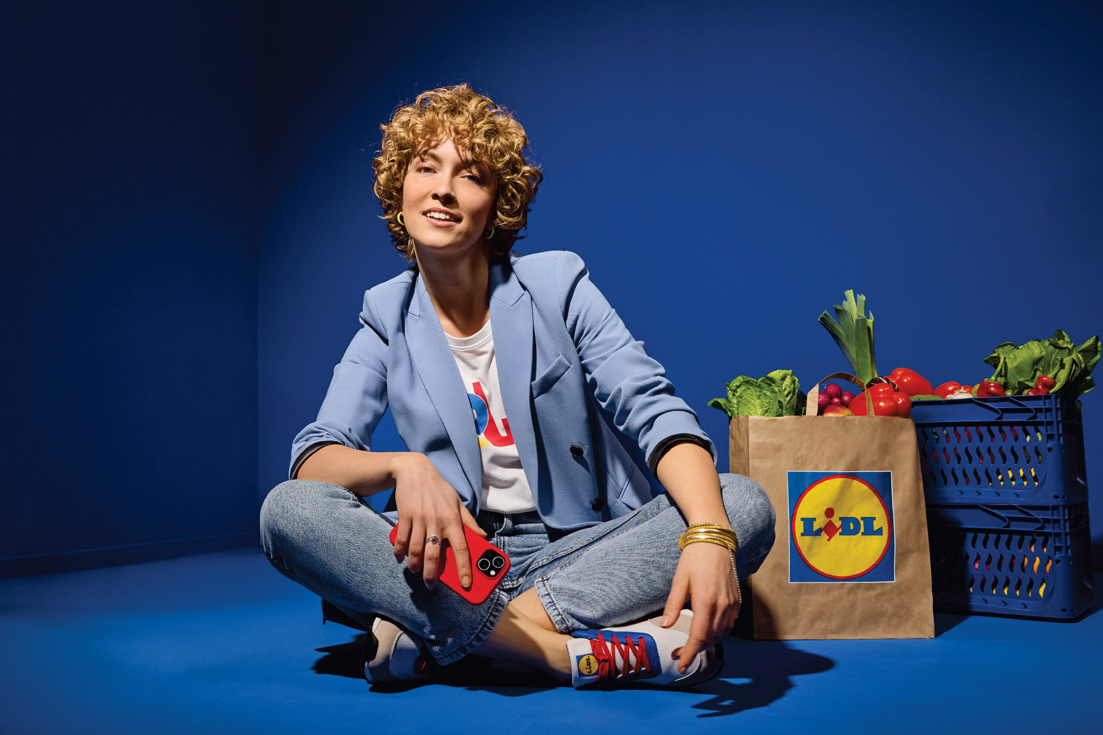 Жена седи на пода с пазарска чанта на Lidl, пълна с пресни зеленчуци и плодове.