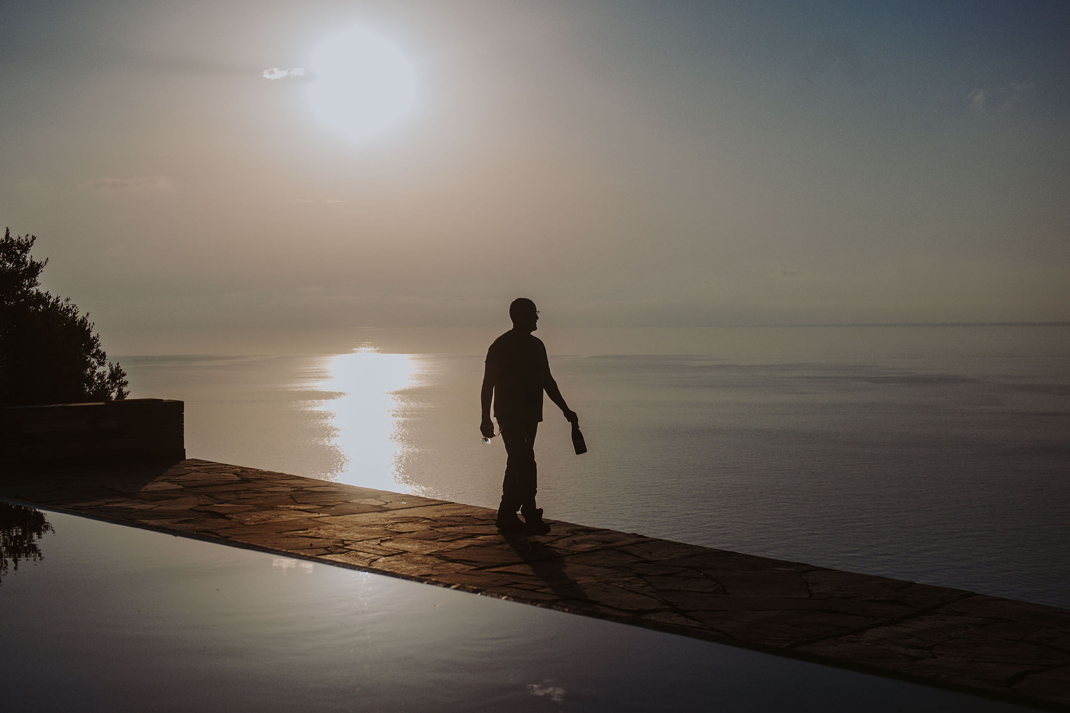 Силует на човек с бутилка и чаша до инфинити басейн по залез слънце