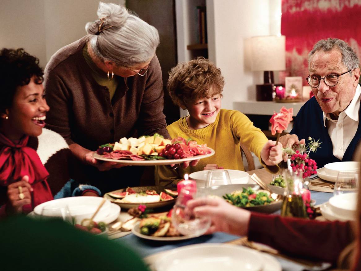 Семейство се наслаждава на вечеря, включваща плато със сирена и колбаси.