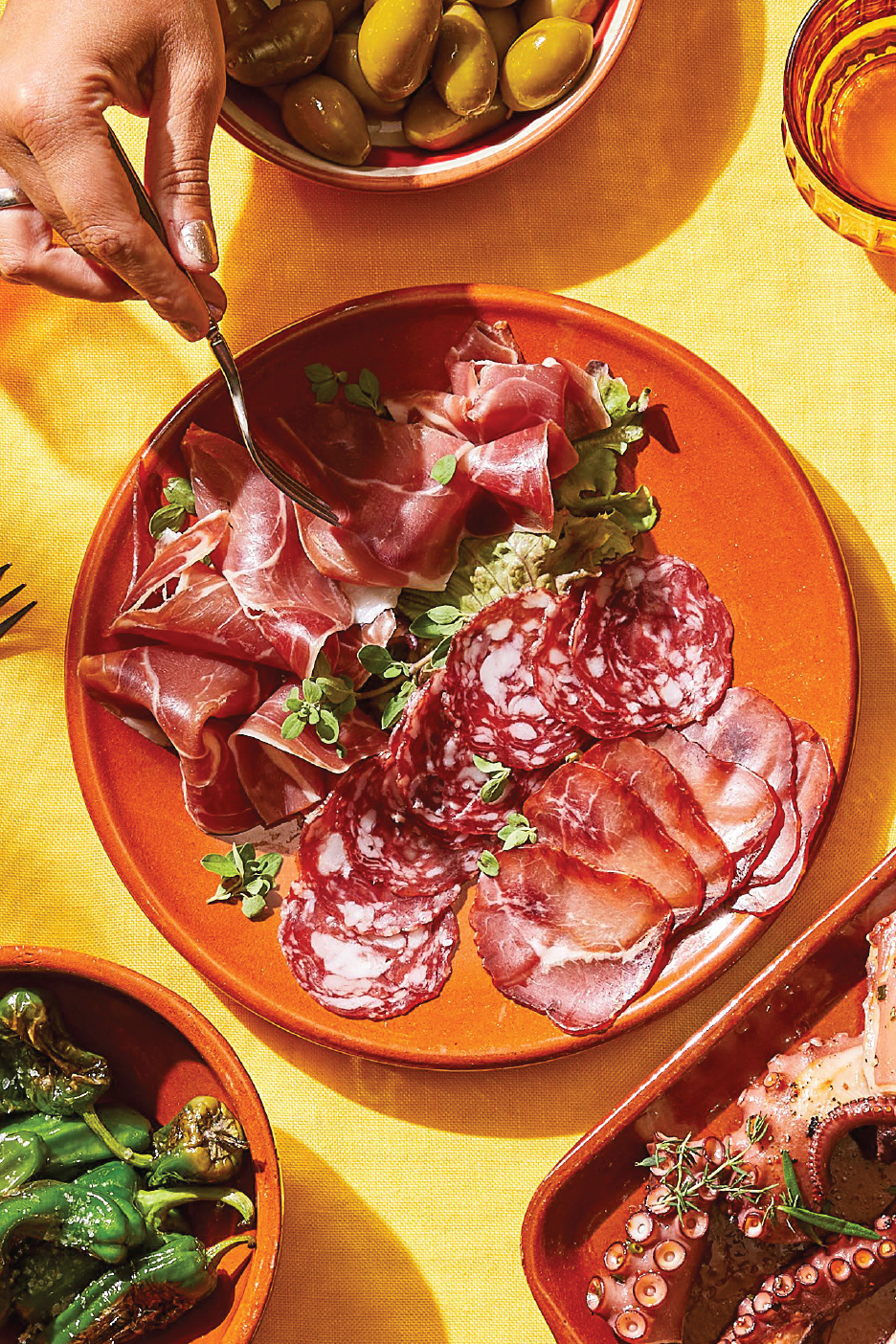 Чиния с прошуто, салам и други колбаси, маслини, чушки и октопод на маса.