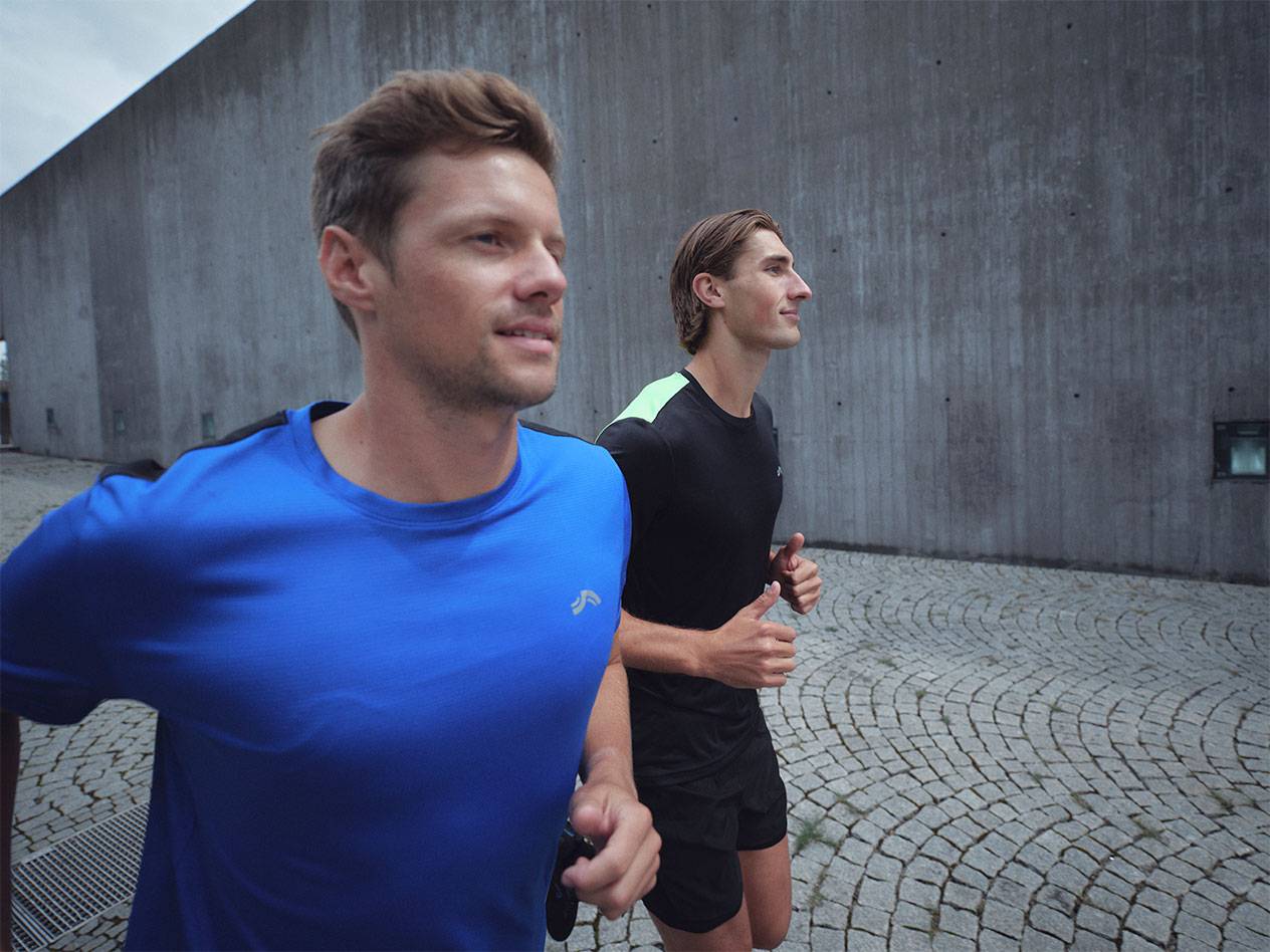 Двама мъже тичат в спортни тениски и къси панталони, един син и един черен.