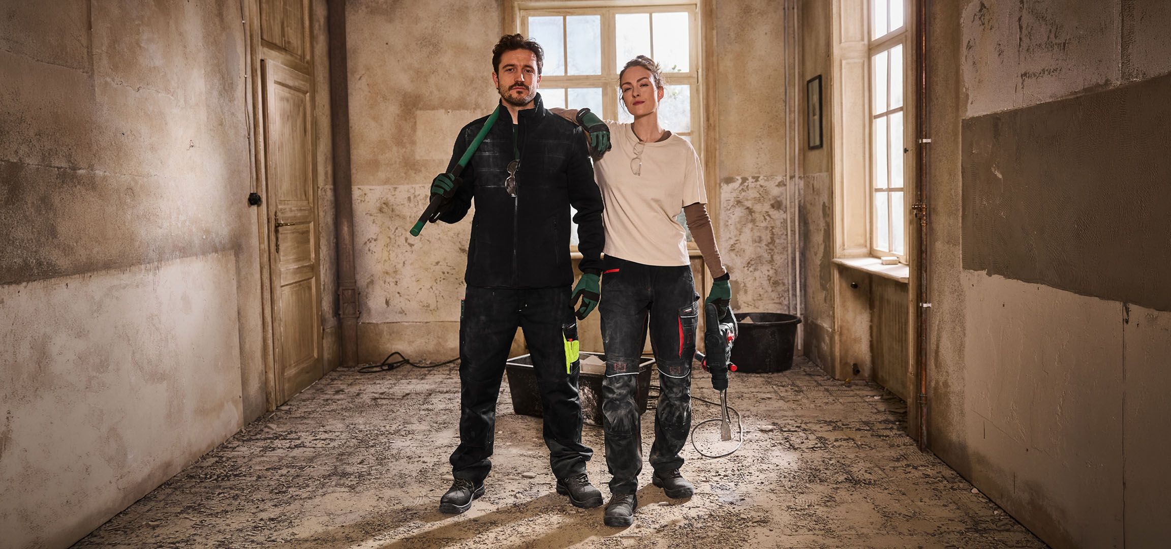 Двама строителни работници в работно облекло с инструменти на строителна площадка.