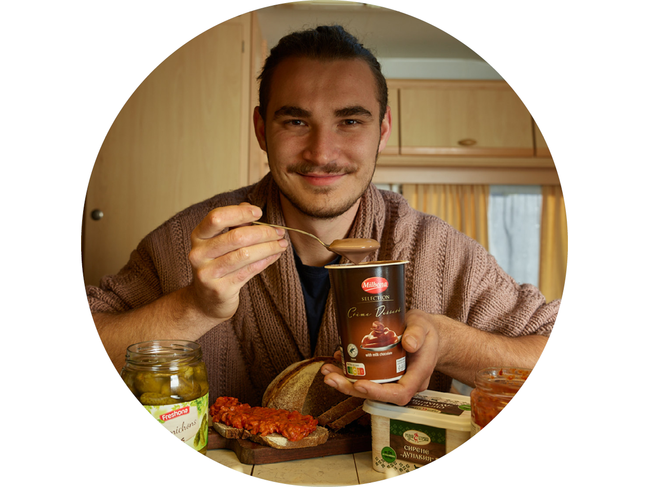 Мъж яде Milbona Selection Crème Dessert, до него кисели краставички и лютеница.