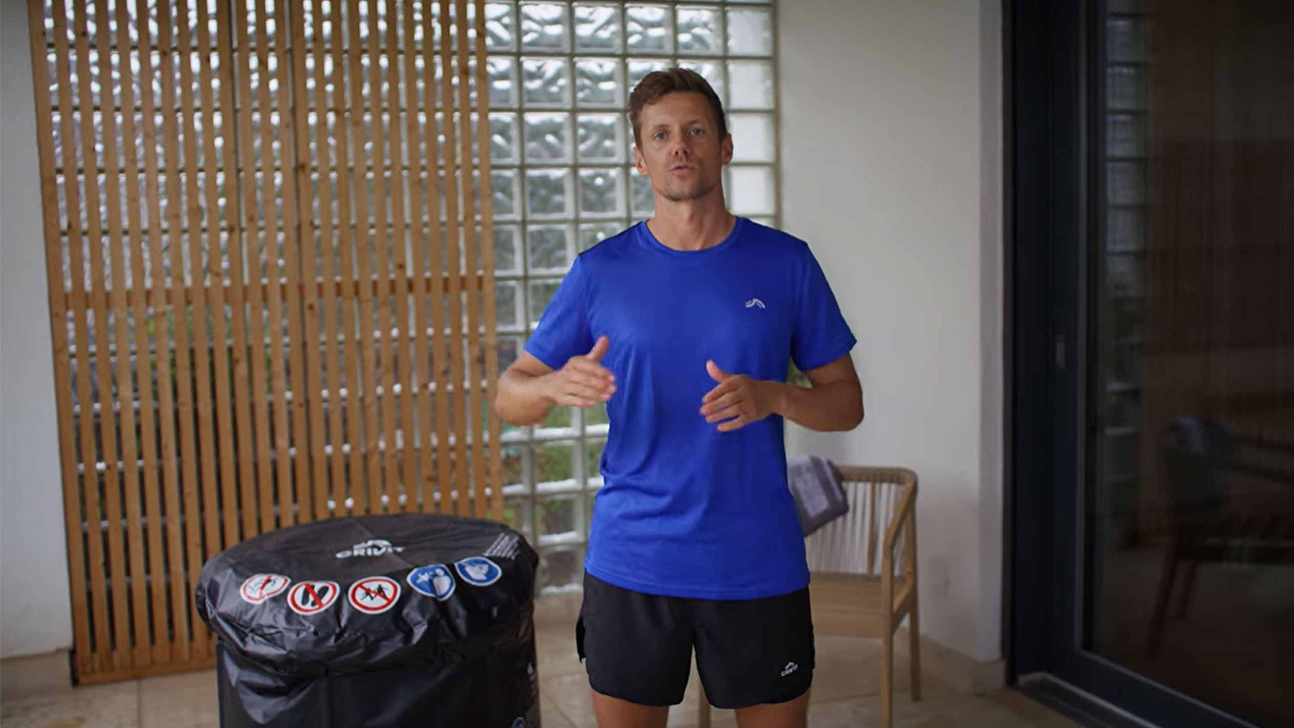 Мъж в синя тениска и черни шорти, до черен капак за джакузи.