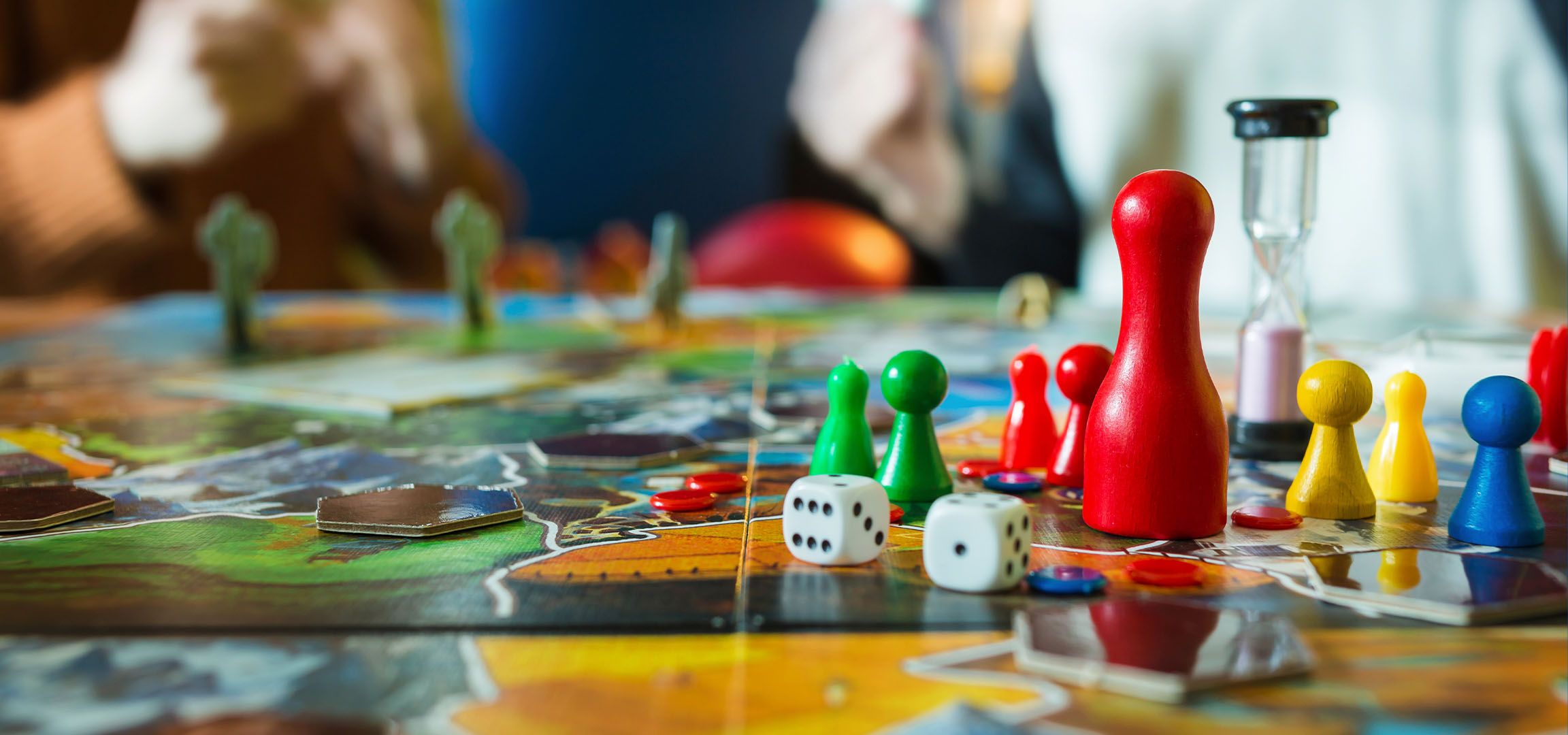 Цветни фигури за настолна игра, включително червени, зелени, жълти и сини пионки, със зарове.