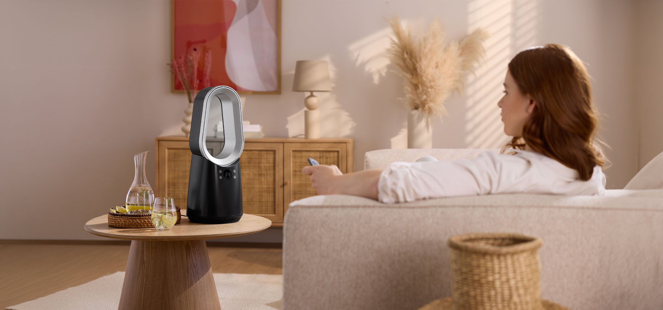 Жена на диван с дистанционно, модерен вентилатор и напитки на маса.