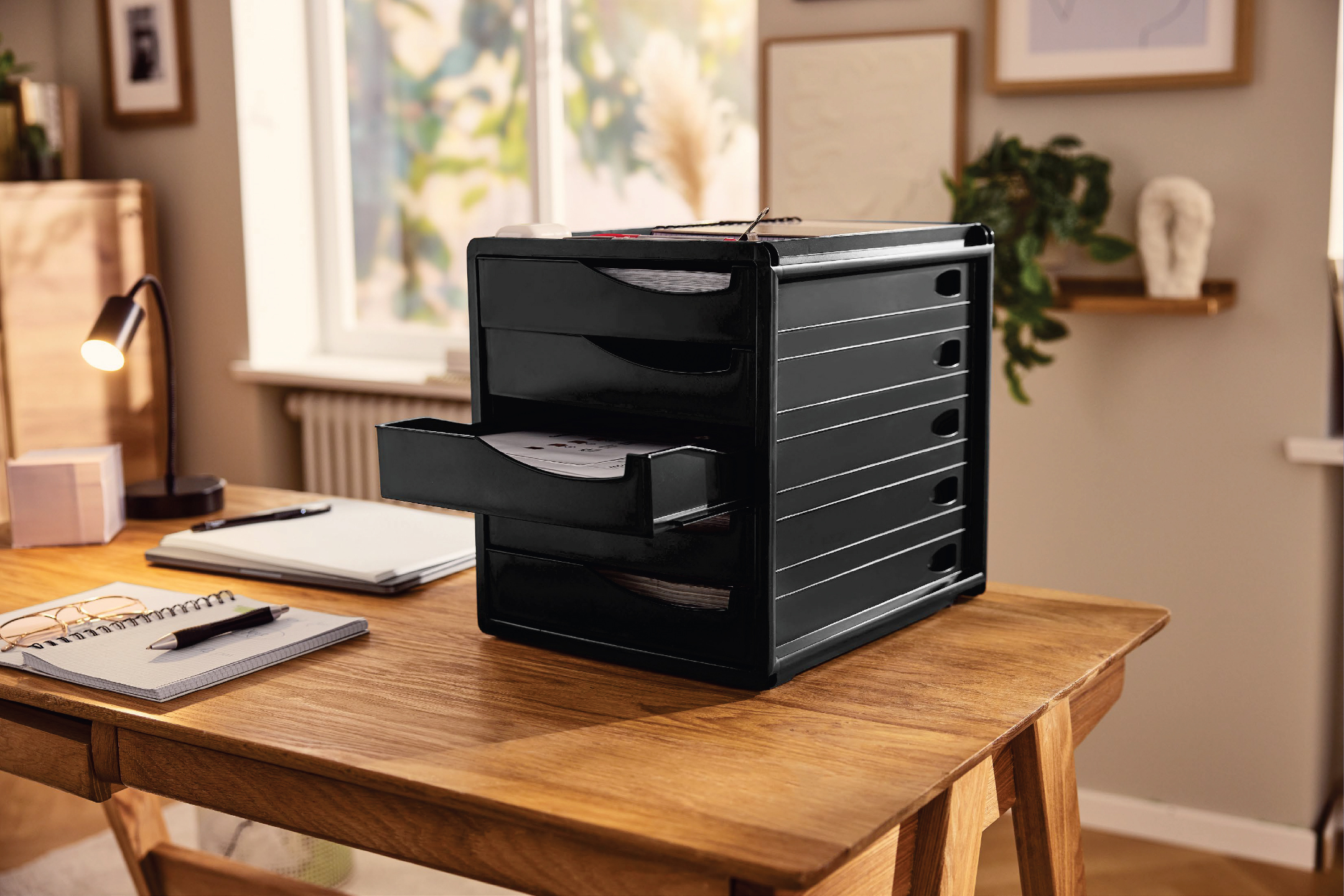 Черен настолен органайзер с чекмеджета, тетрадки и лампа на дървено бюро.