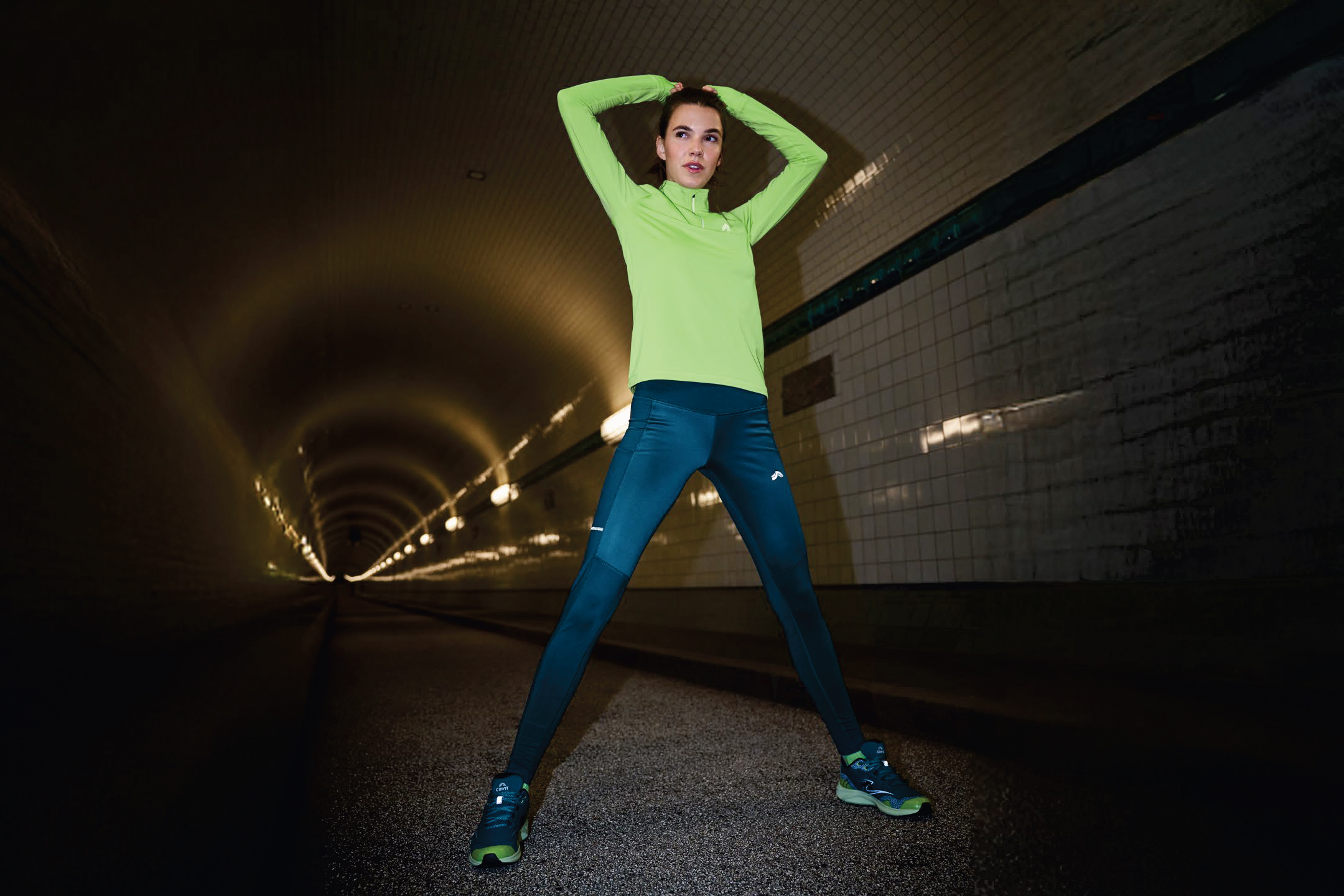 Жена в неоновозелена спортна блуза и тъмносини клинове в тунел.