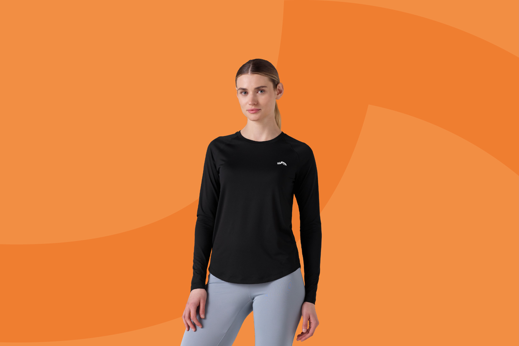 Жена в черна спортна блуза с дълъг ръкав и сиви клинове на оранжев фон.