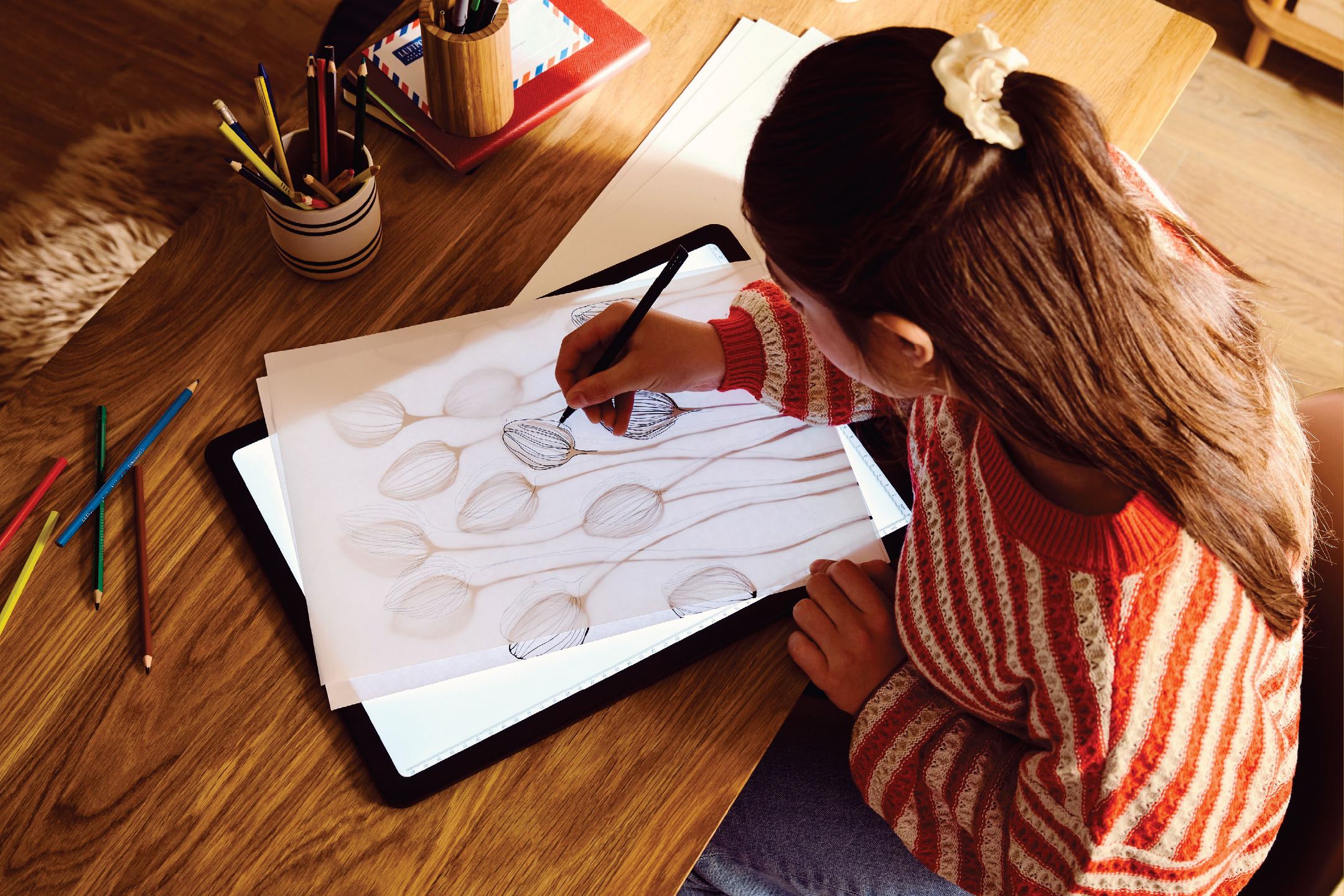 Жена рисува върху светеща дъска с молив, създавайки флорални мотиви.