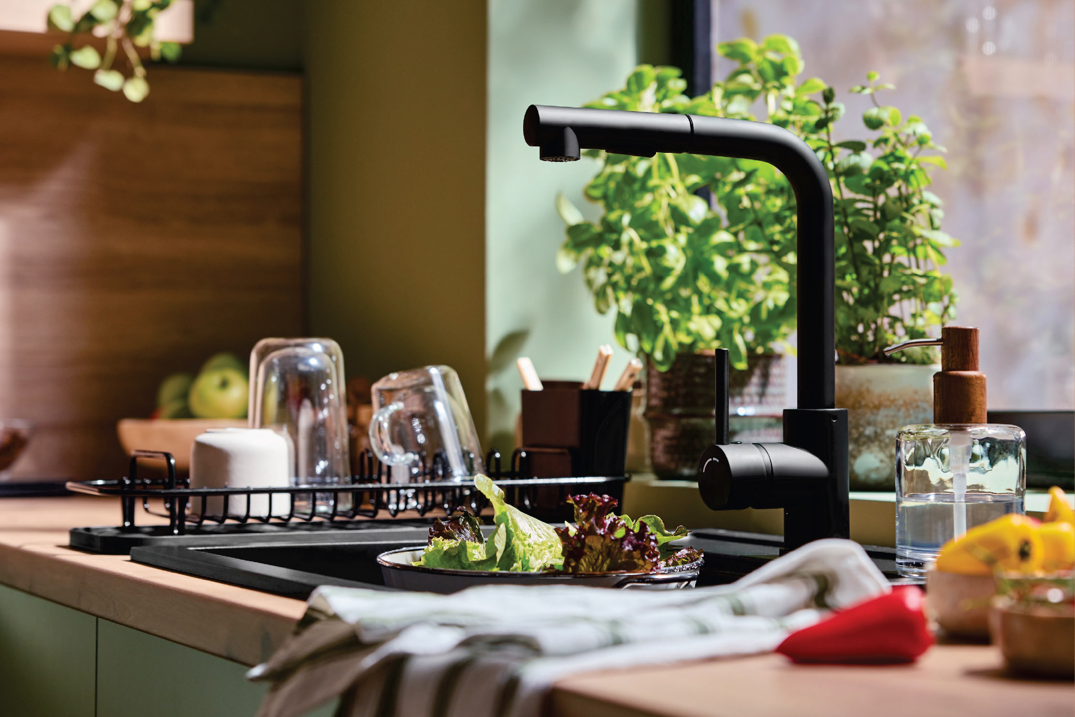 Кухненска мивка с черен смесител, сушилник за съдове и свежи зеленчуци.