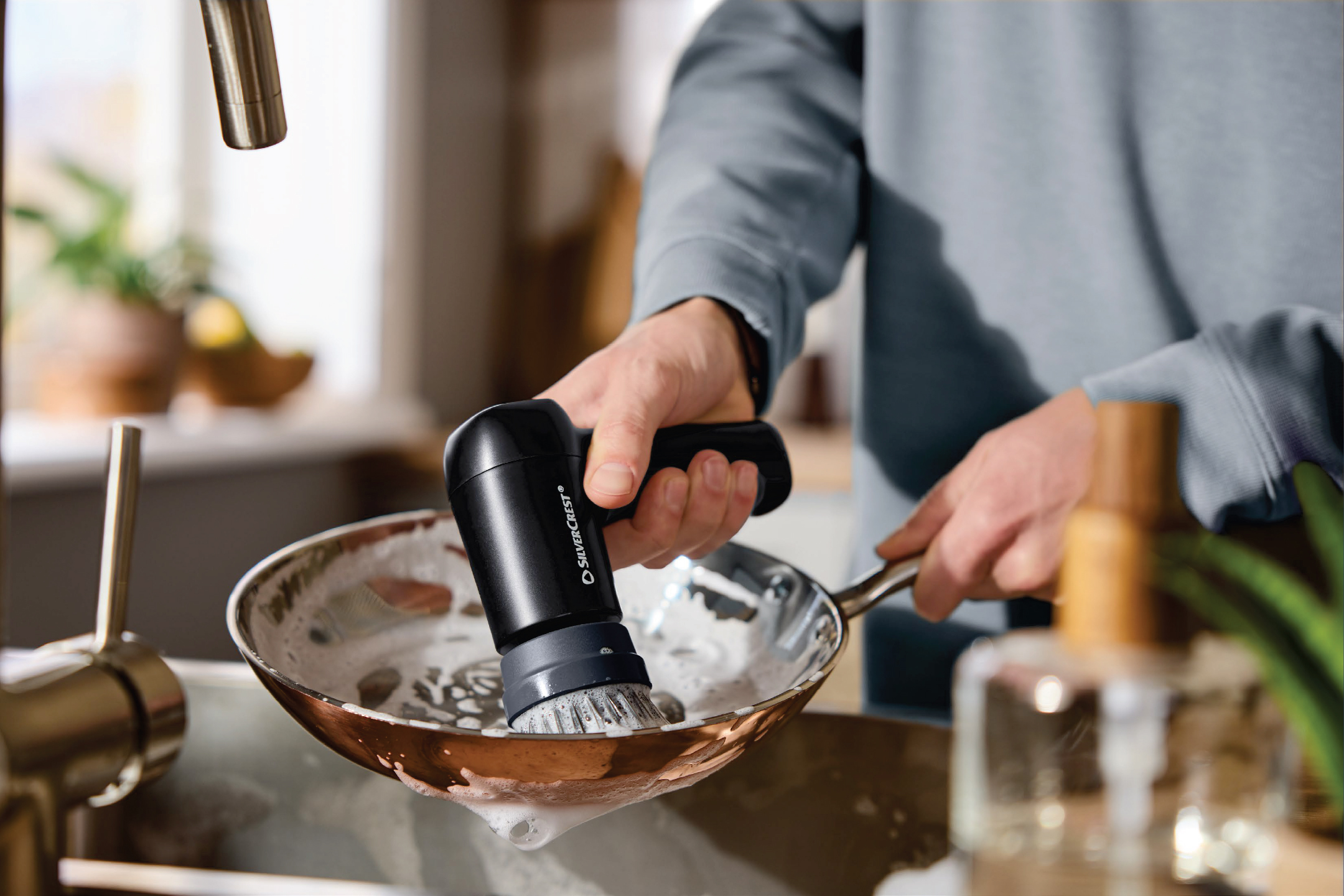 Мъж мие тиган с електрическа четка за съдове в кухнята.