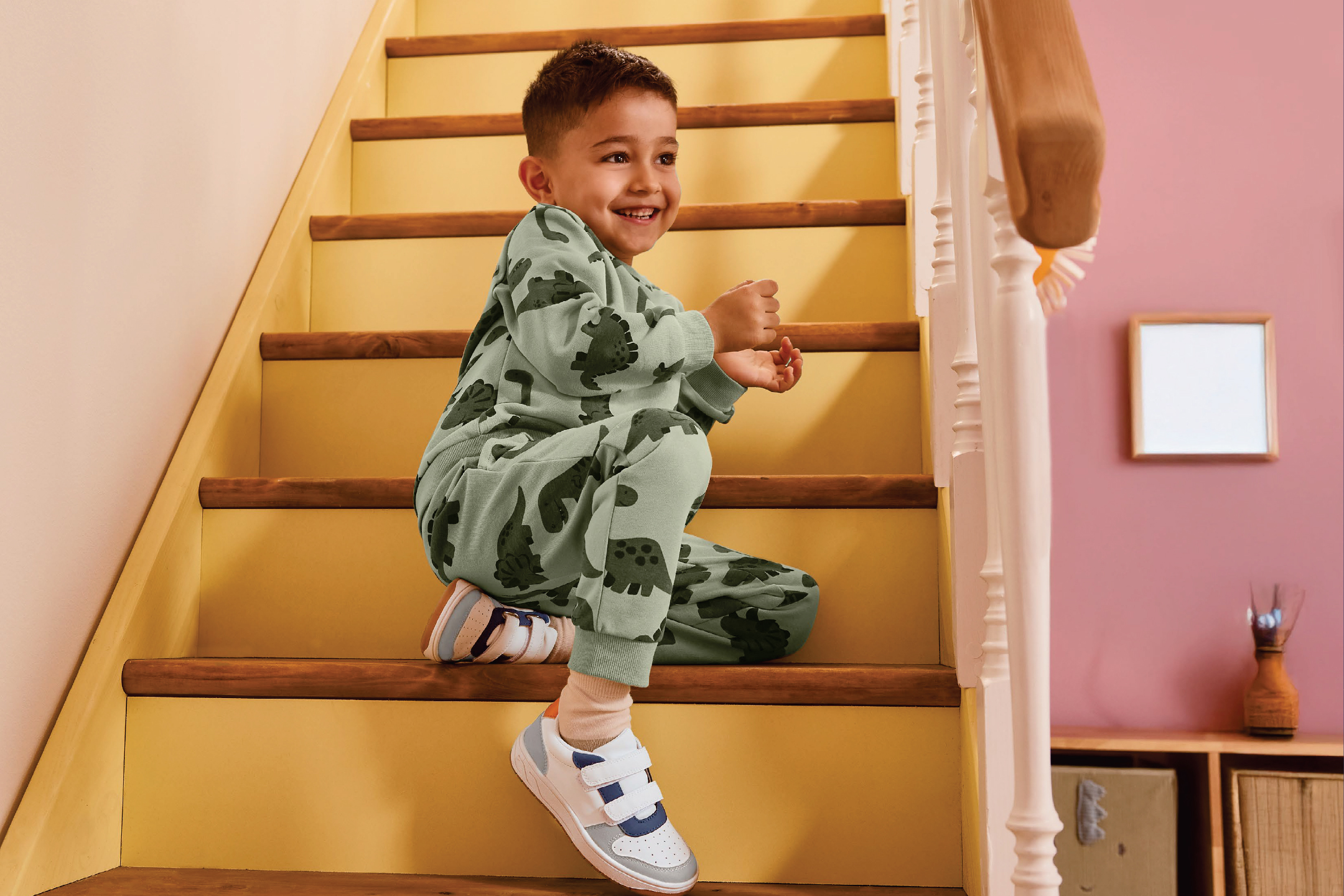 Момче в пижама с динозаври и маратонки седи на стълбите.
