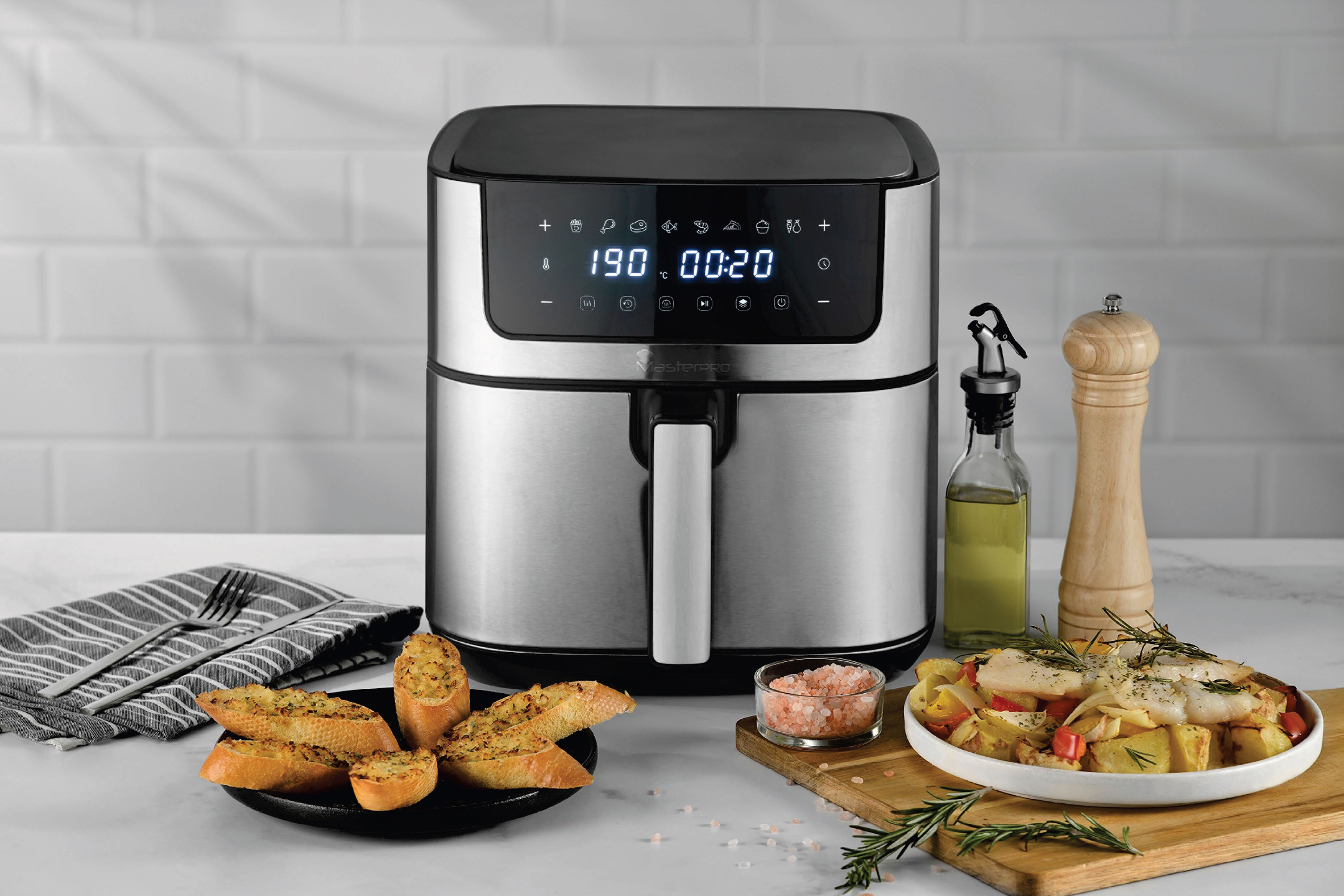 Сребрист фритюрник с горещ въздух Masterpro, чеснови хлебчета и ястие с риба и зеленчуци.