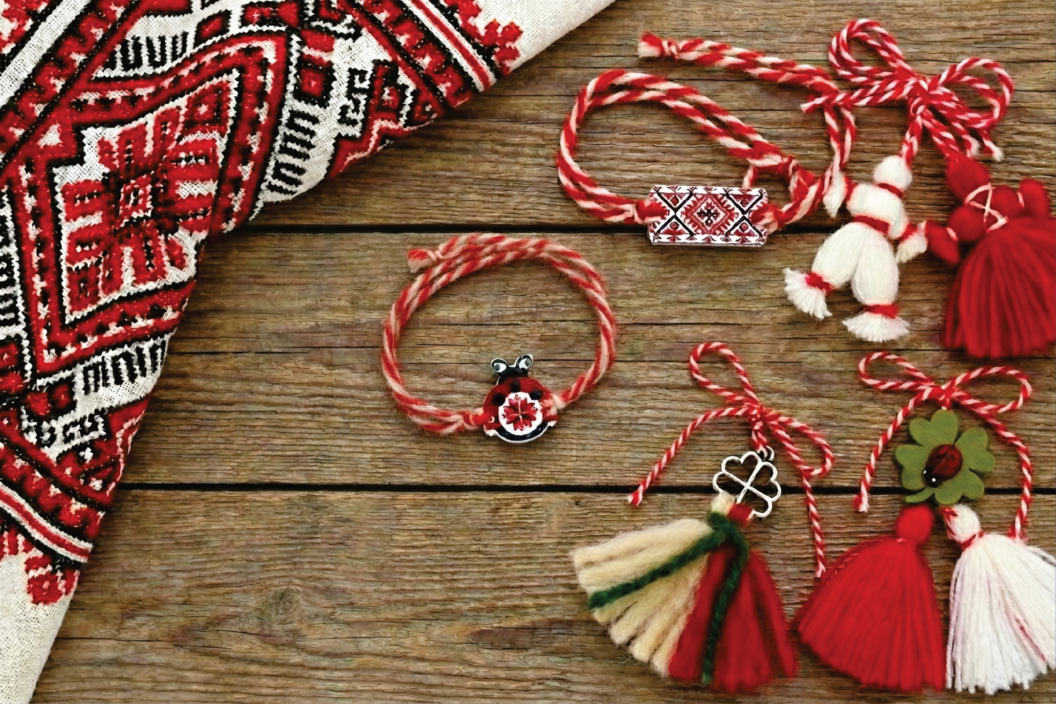 Традиционни мартеници и бродирана кърпа върху дървена повърхност.