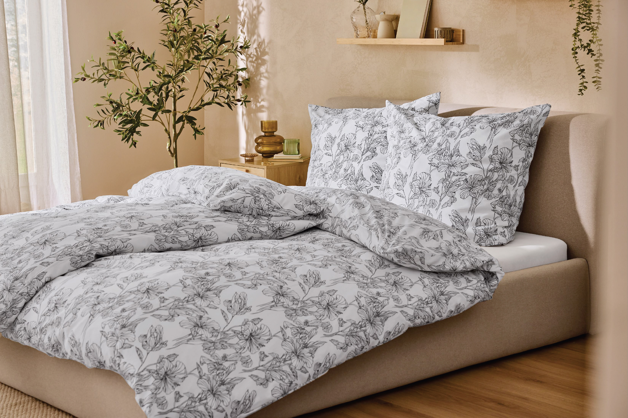 Спалня с бял спален комплект с черни флорални мотиви и нощно шкафче с декорации.