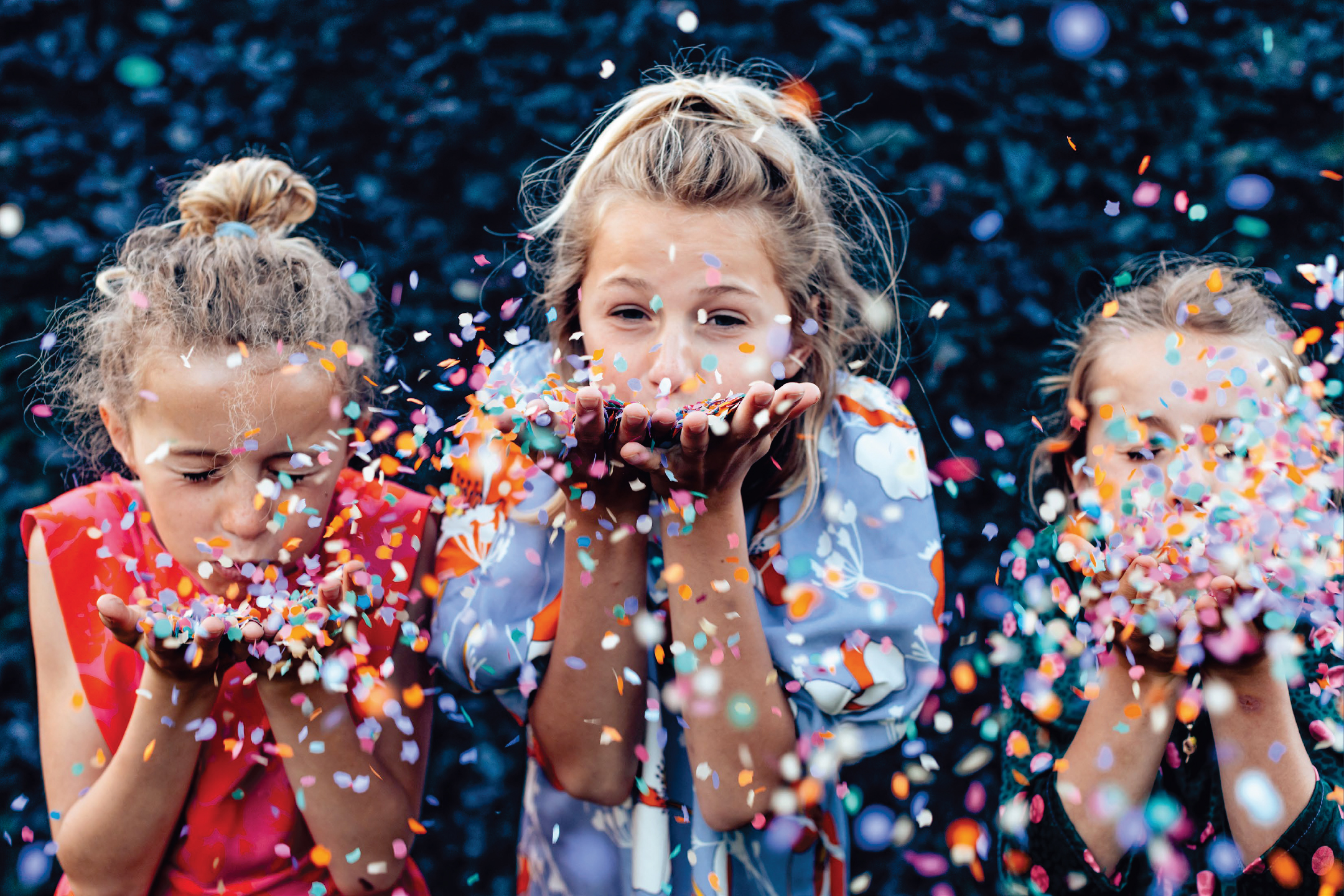 Три деца хвърлят цветни конфети, празнувайки рожден ден или парти.