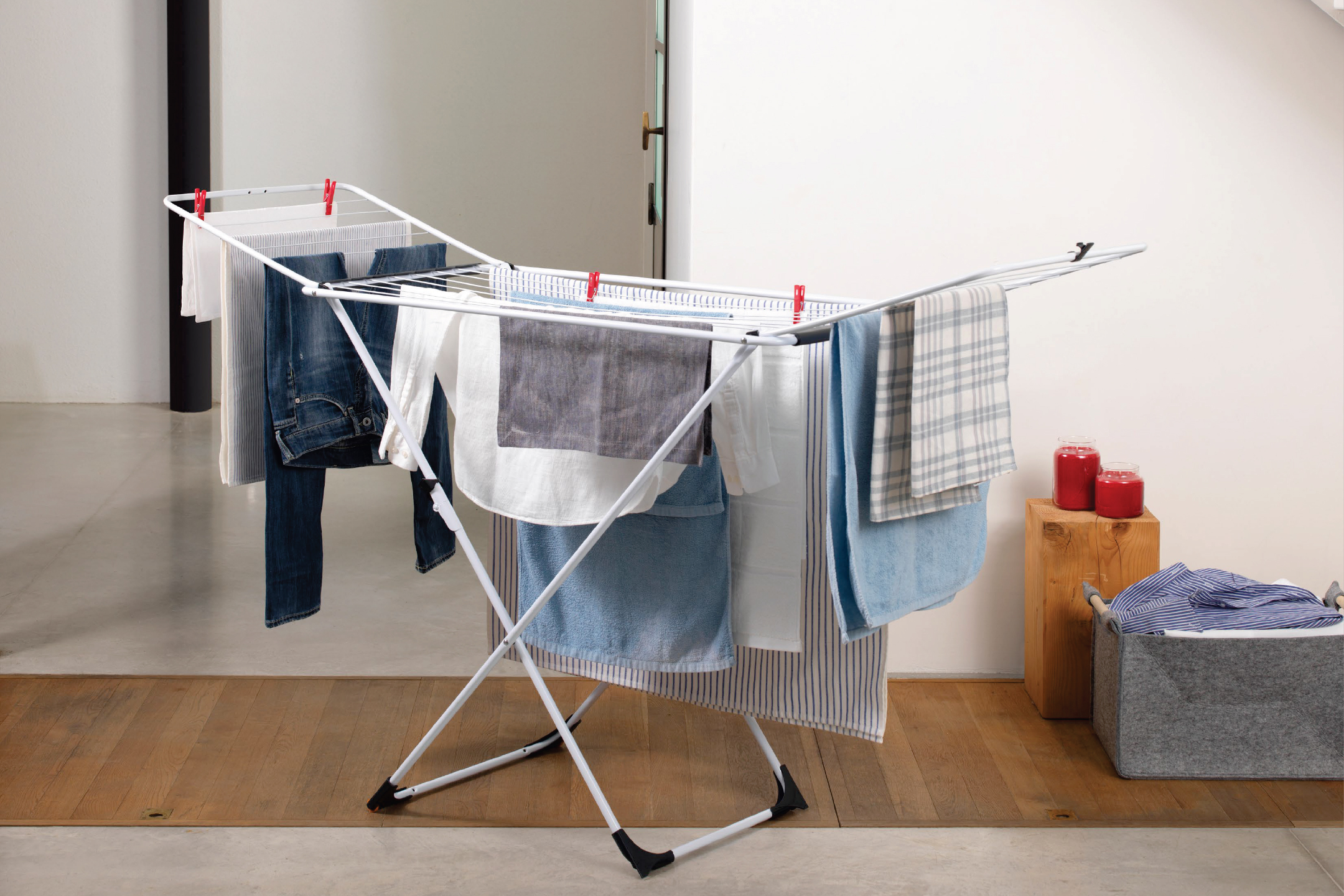 Сушилник за дрехи с различни дрехи, кърпи и кош за пране.