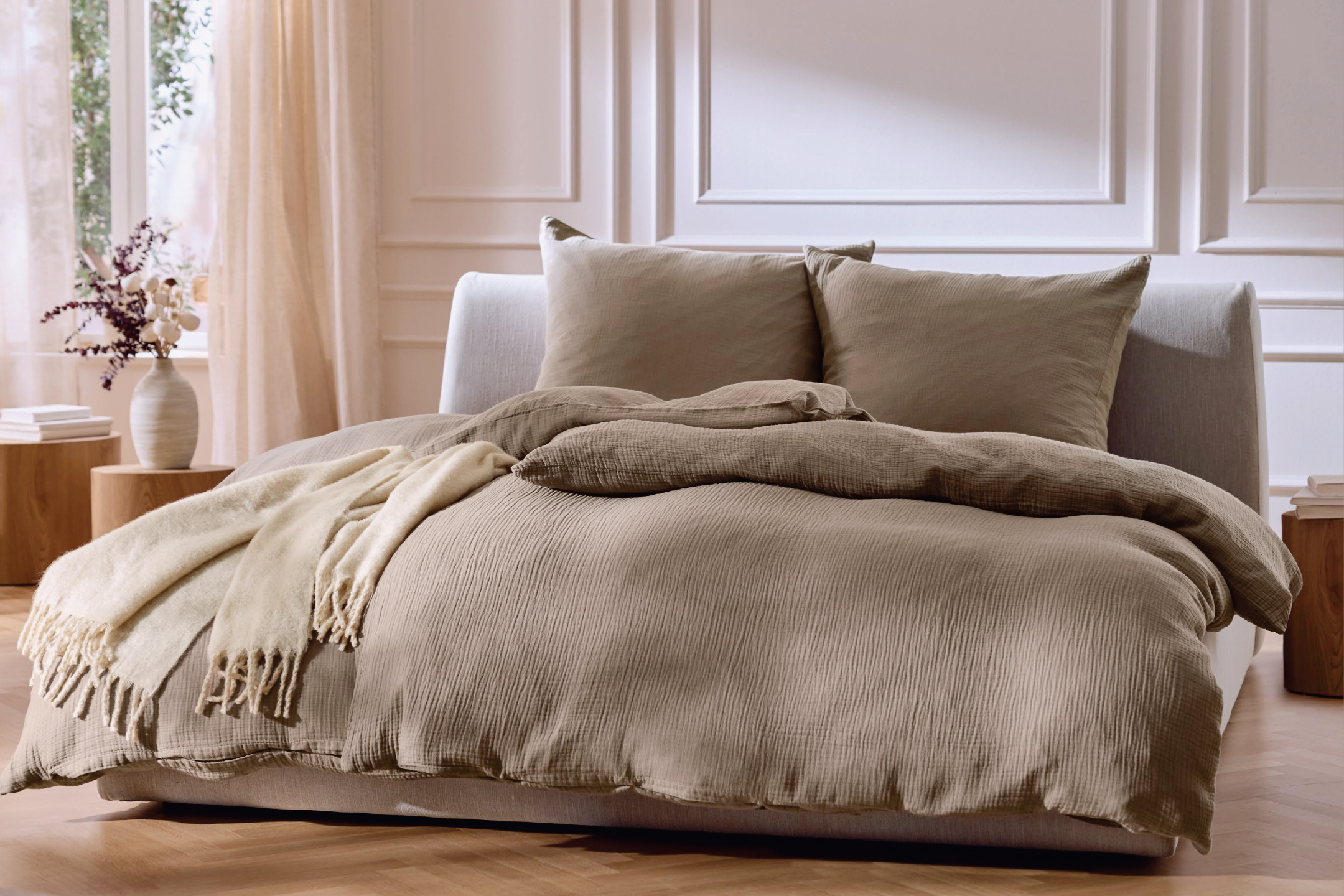 Спалня с бежово спално бельо, възглавници и одеяло, с нощни шкафчета и лампа.