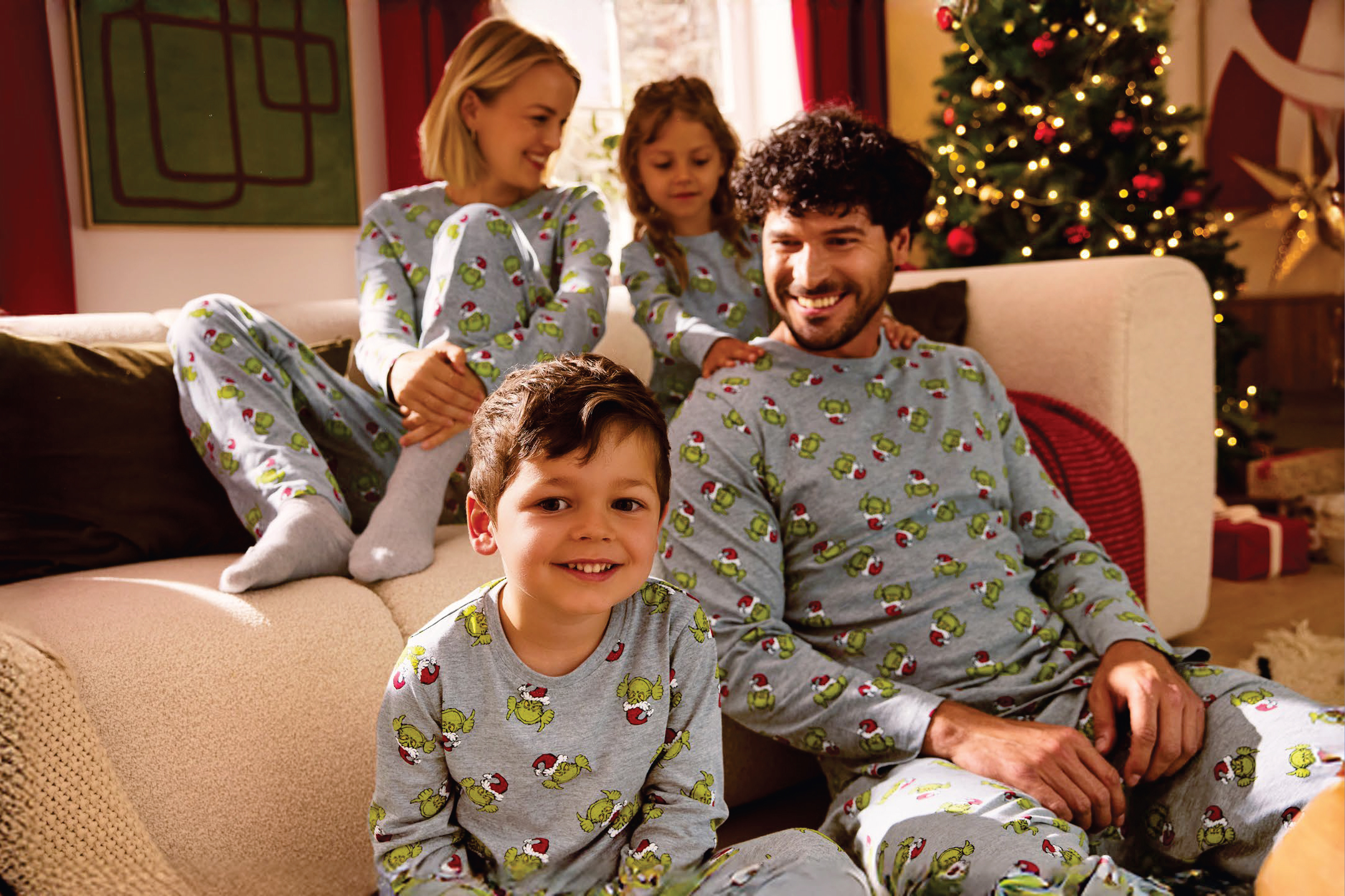 Семейство в еднакви коледни пижами Grinch, седнало на диван до коледна елха.