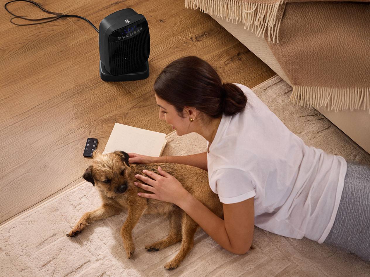 Жена гали куче до черен отоплител на пода.