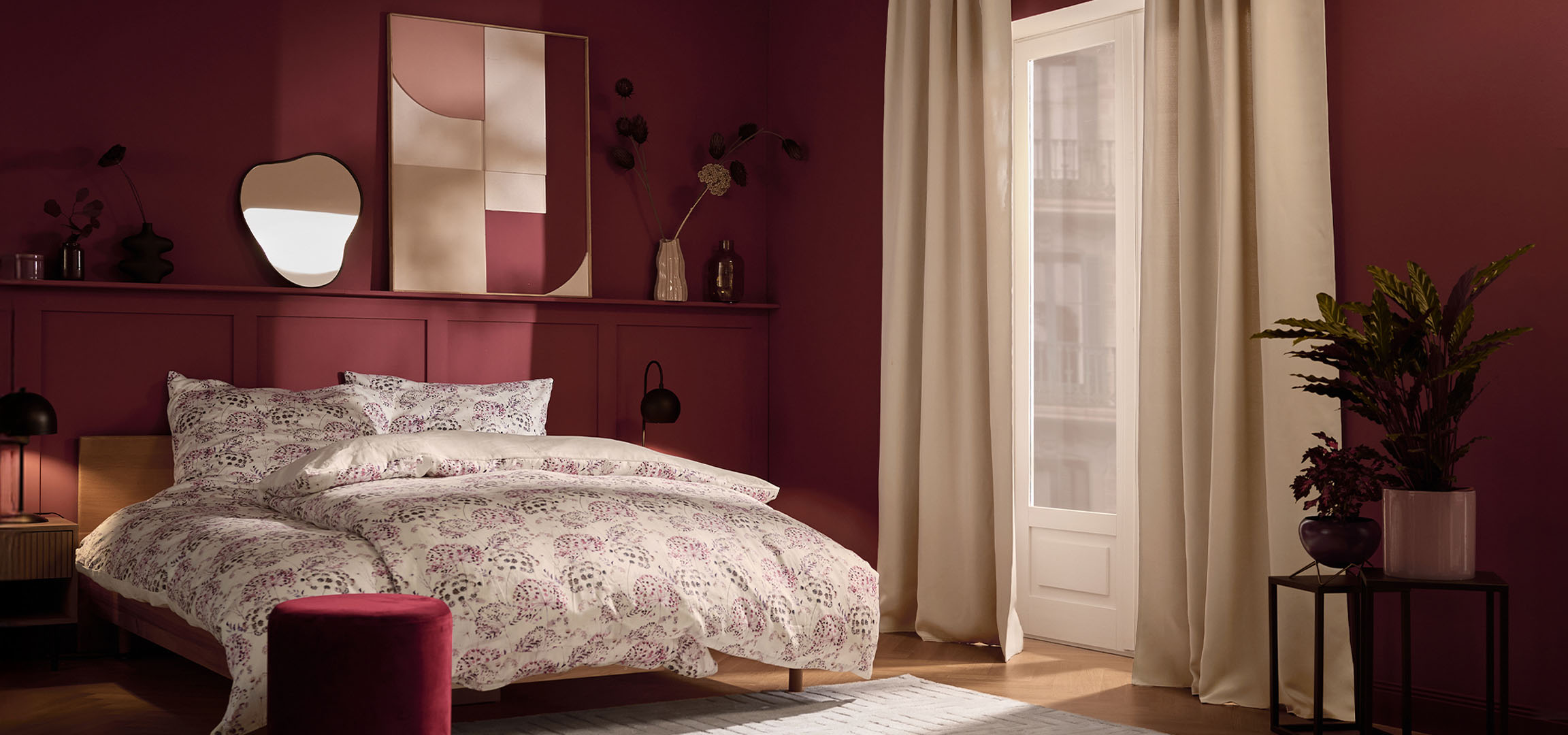Спалня с бордо стени, легло с бяло спално бельо с флорален десен и растения.