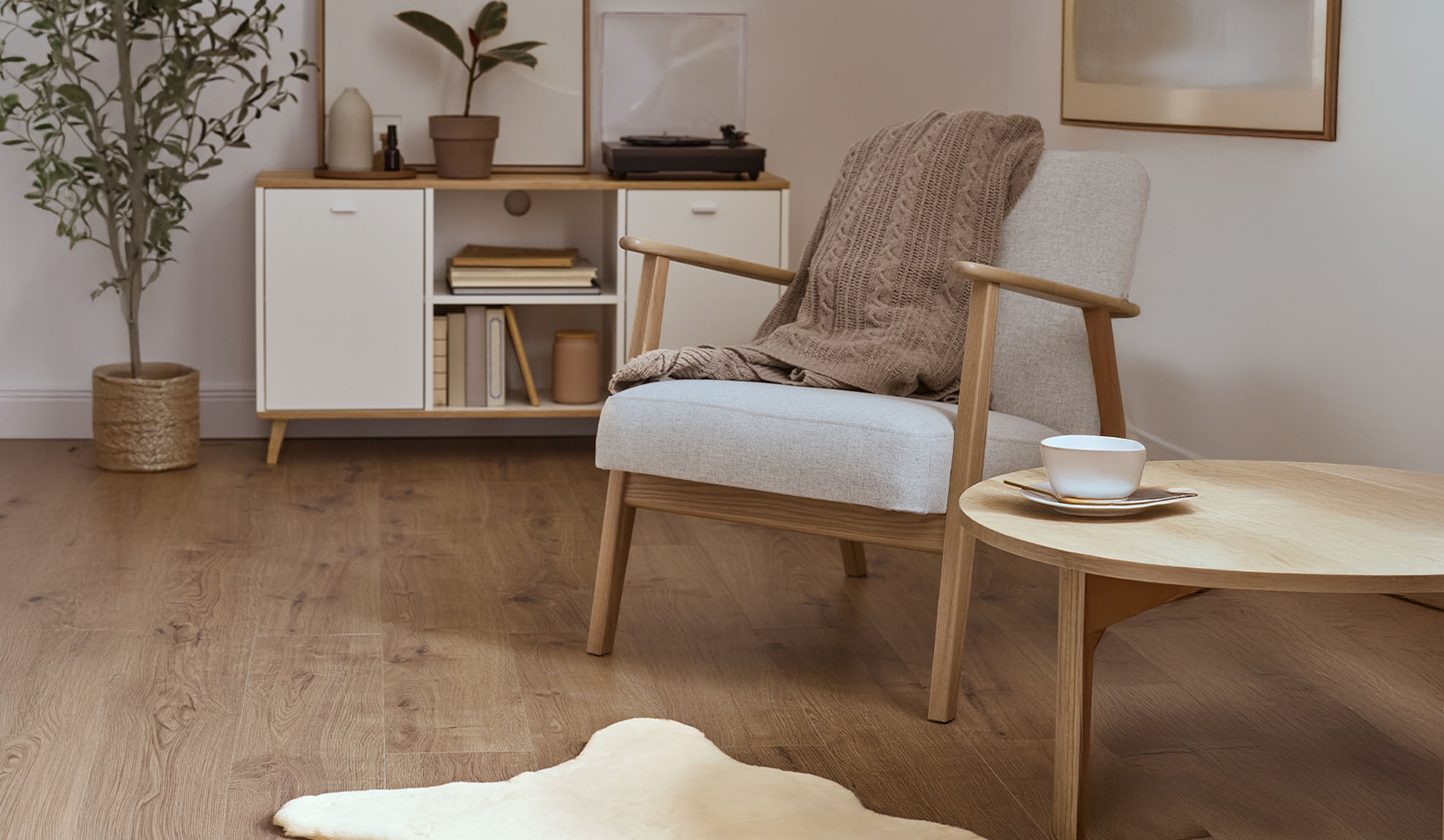 Удобен фотьойл с одеяло, дървена масичка за кафе и шкаф за съхранение в светла всекидневна.