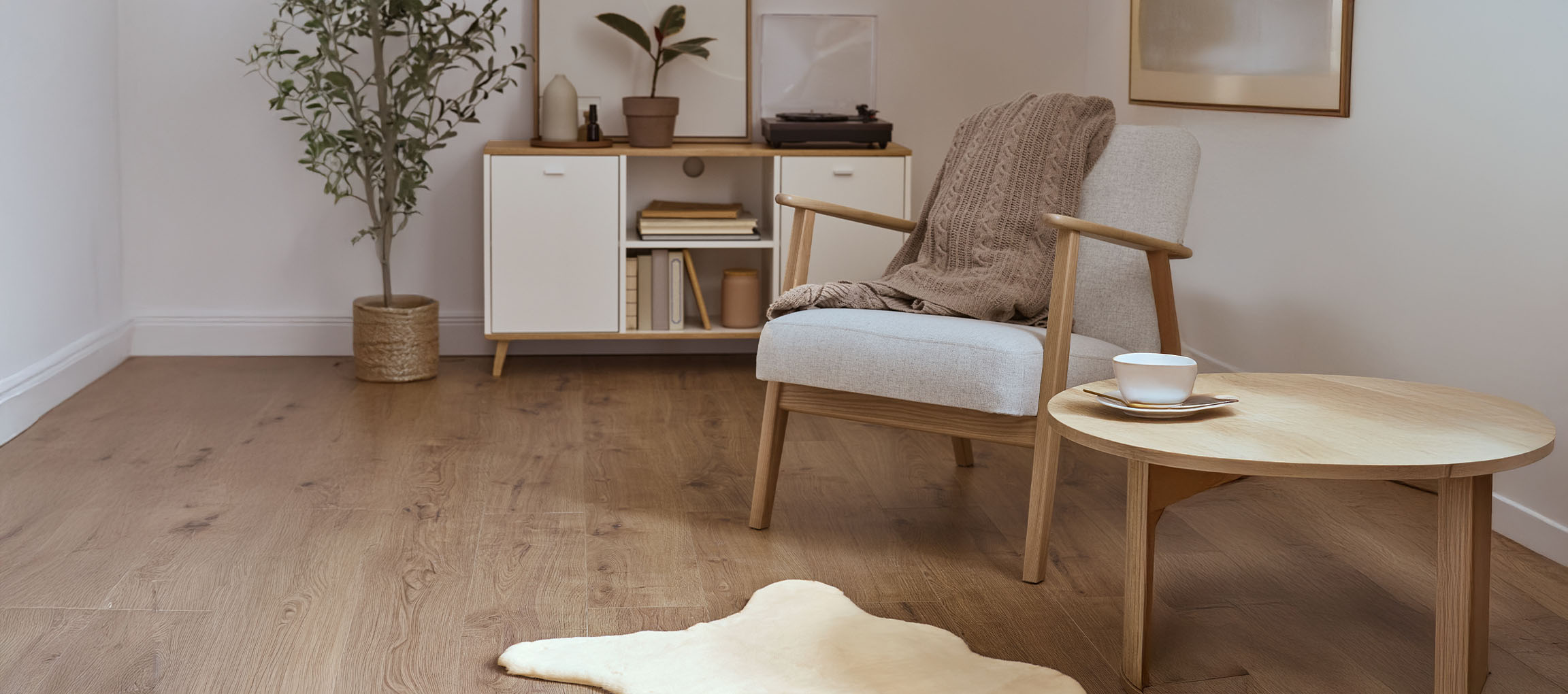 Сив текстилен фотьойл с плетено одеяло, дървена масичка за кафе и модерен бюфет.