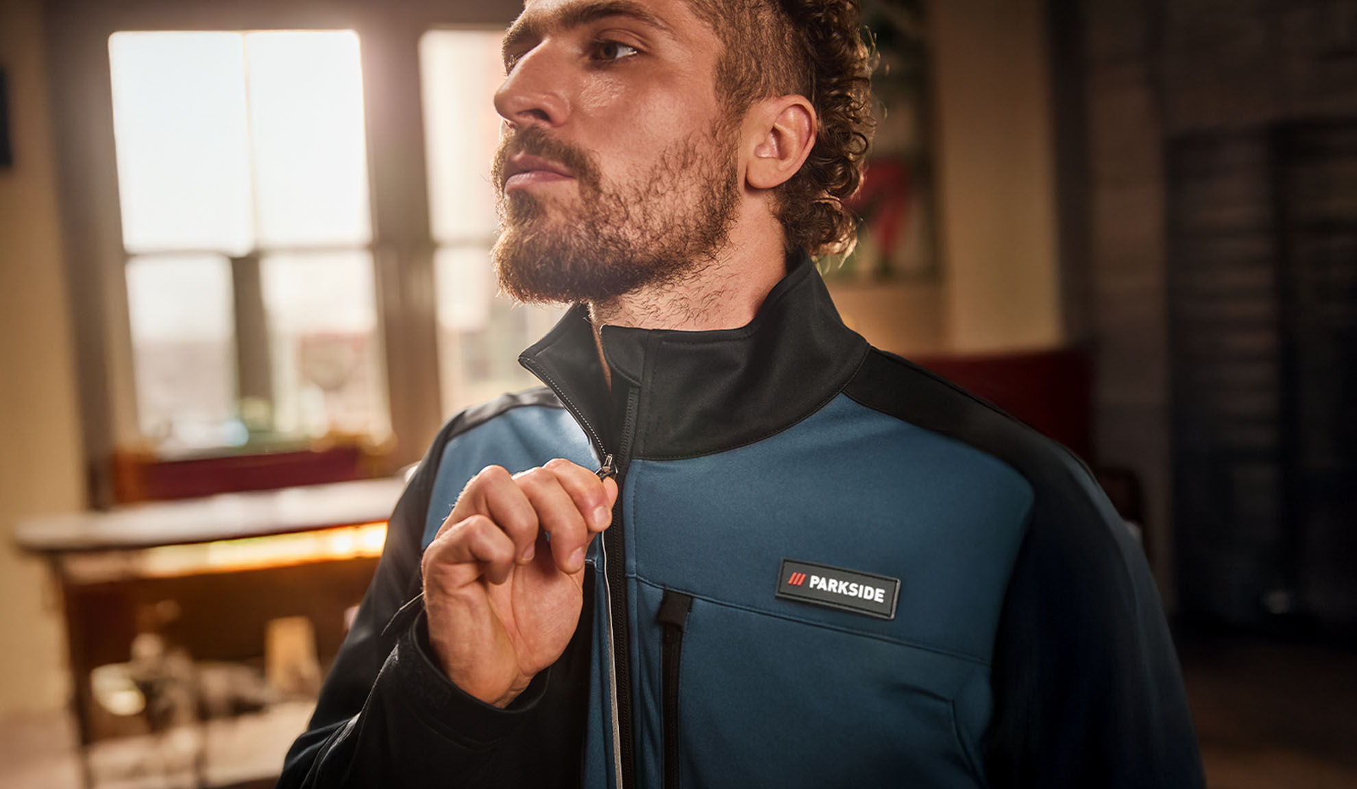 Мъж в синьо-черно работно яке Parkside, закопчаващ го.