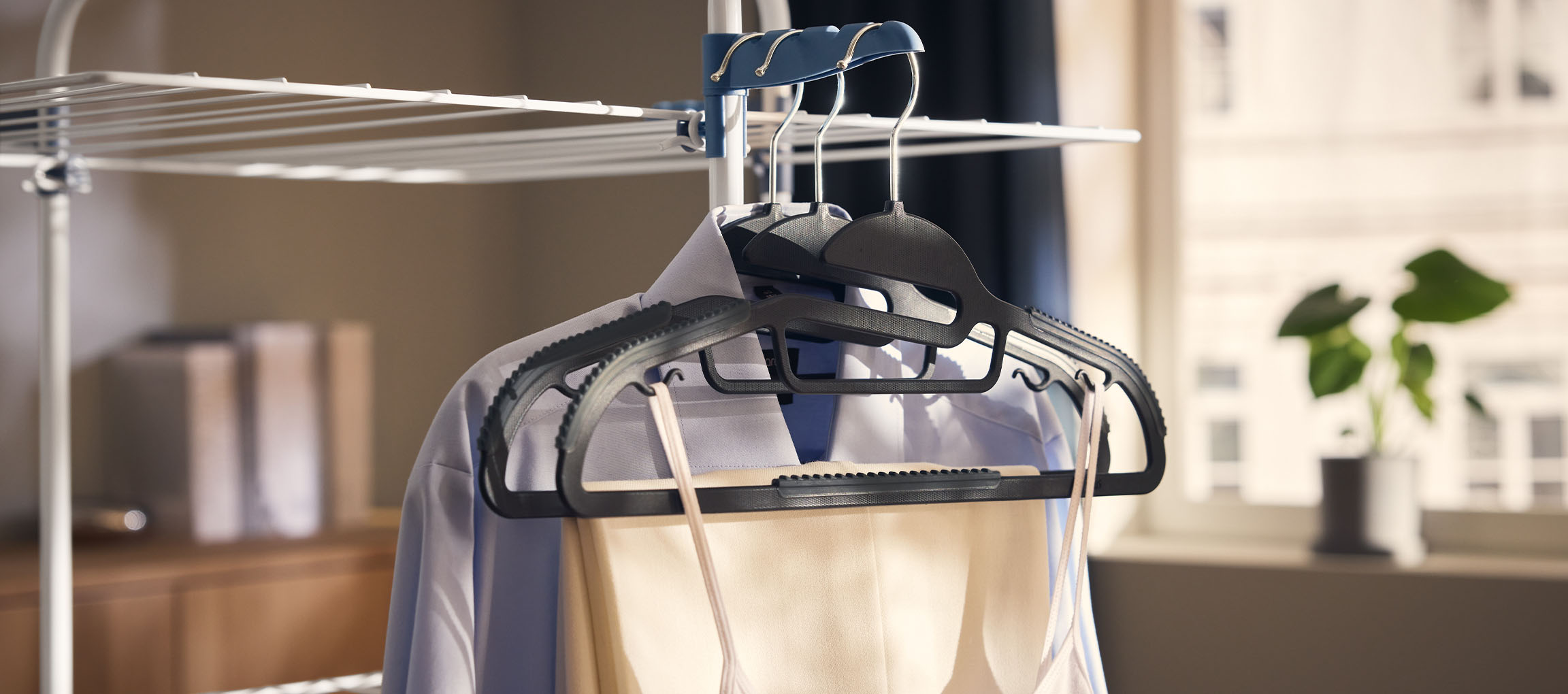 Дрехи на закачалки на сушилник, с растение на заден план.