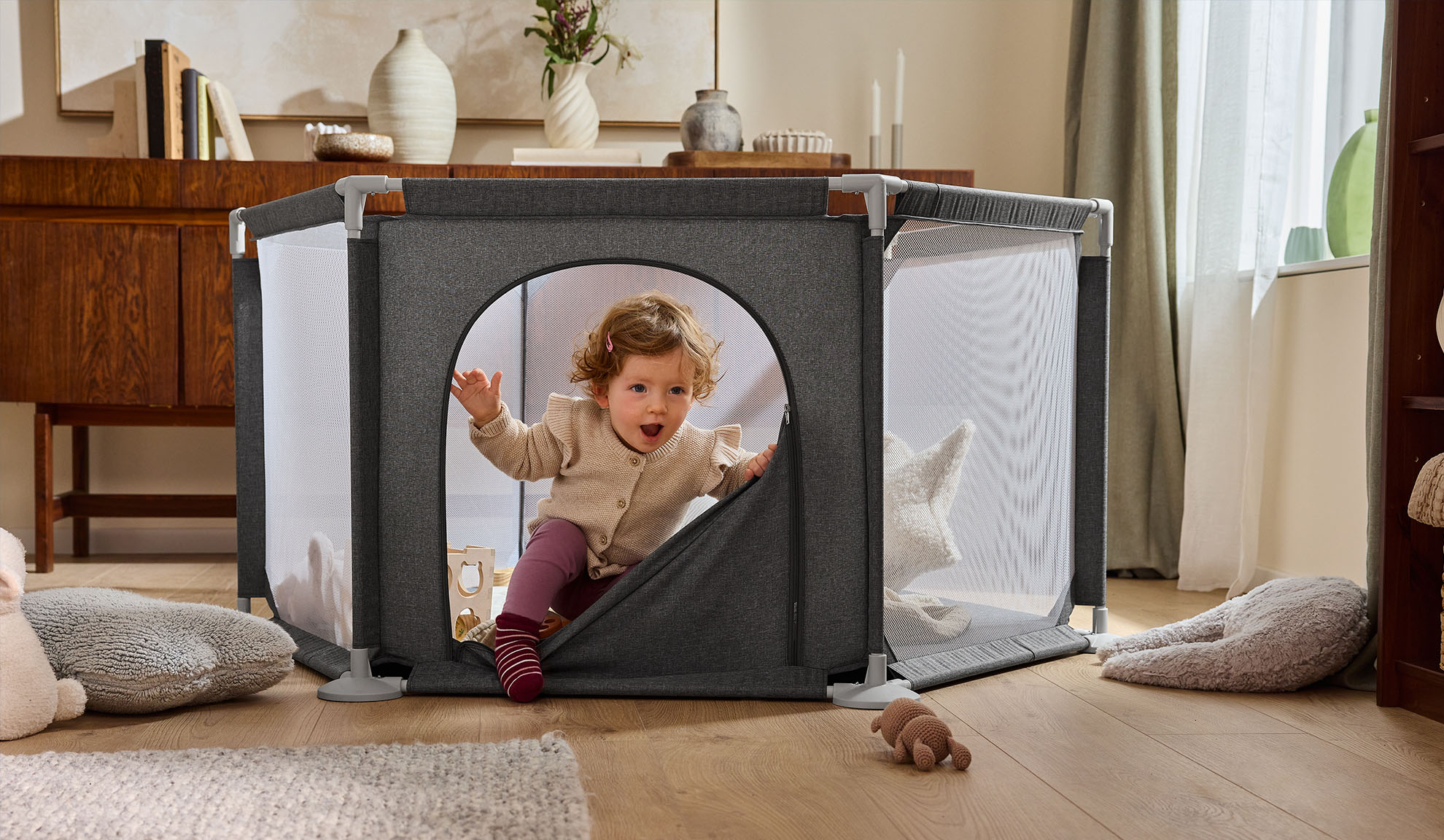 Щастливо бебе излиза от сива кошара в уютна всекидневна.