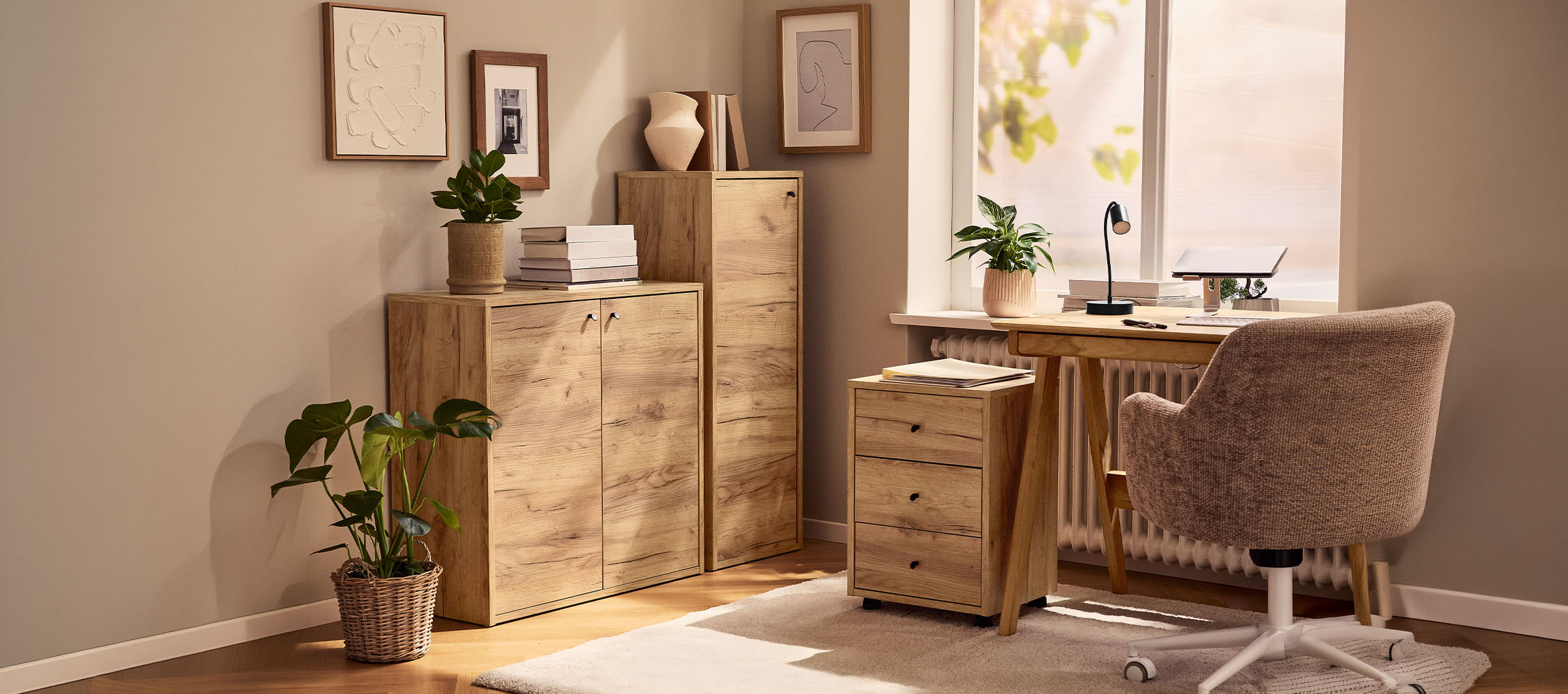 Домашен офис с дървени шкафове, бюро и стол, декориран с растения и картини.