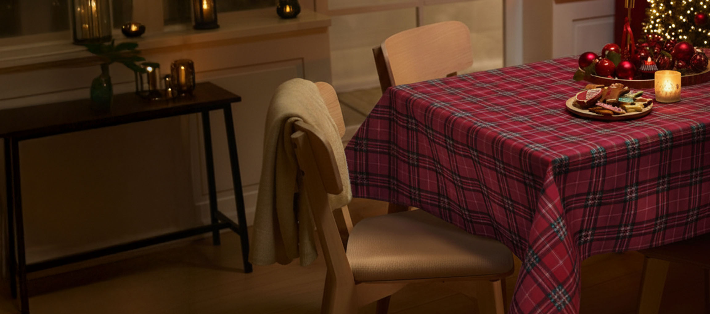 Коледна трапеза с червена карирана покривка, столове и коледни сладки.