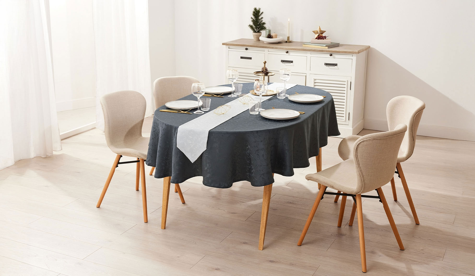 Овална трапезна маса с тъмна покривка, бял тишлайфер и четири бежови стола от плат.