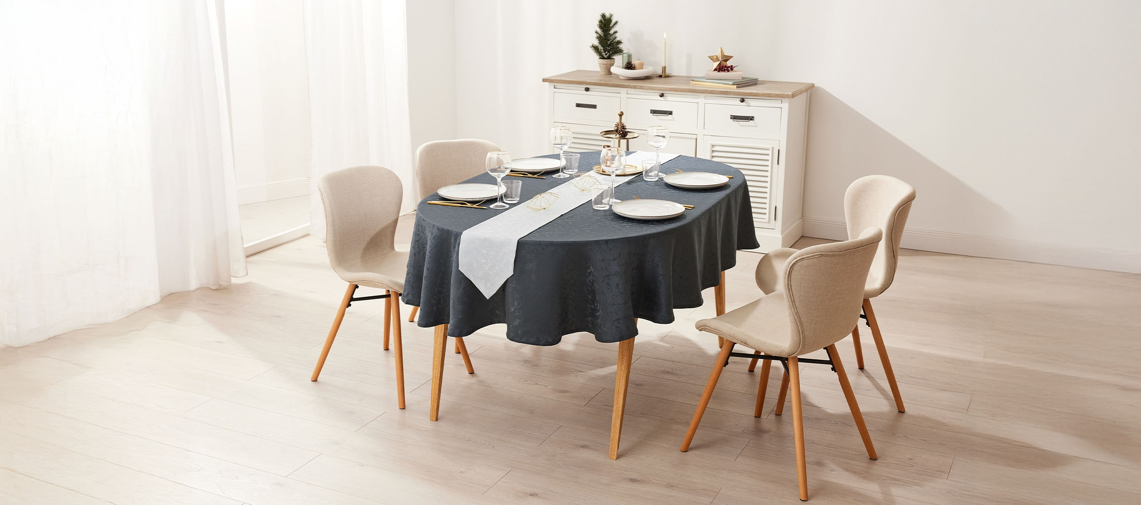 Овална трапезна маса със сива покривка, бял тишлайфер и четири бежови стола.