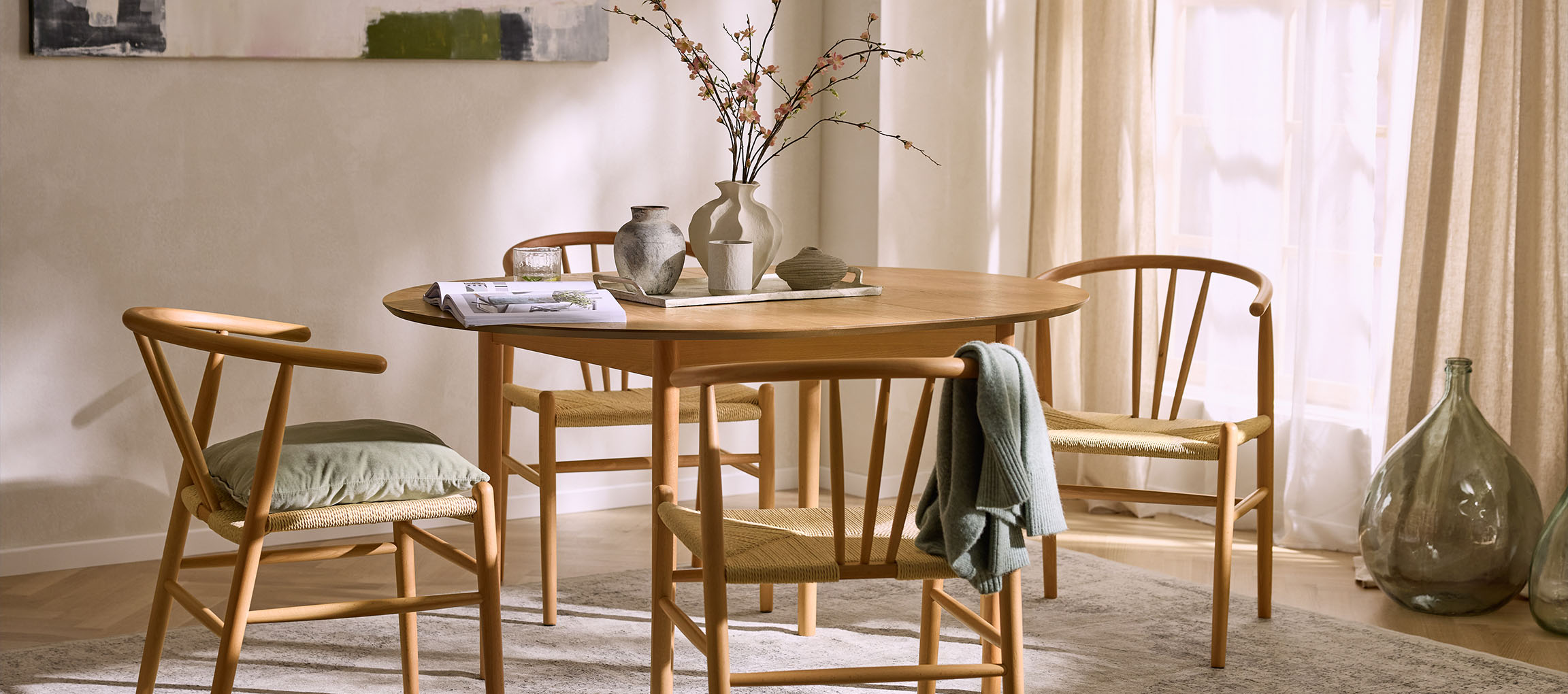 Трапезария с кръгла дървена маса, дървени столове с въжени седалки и декоративни вази.