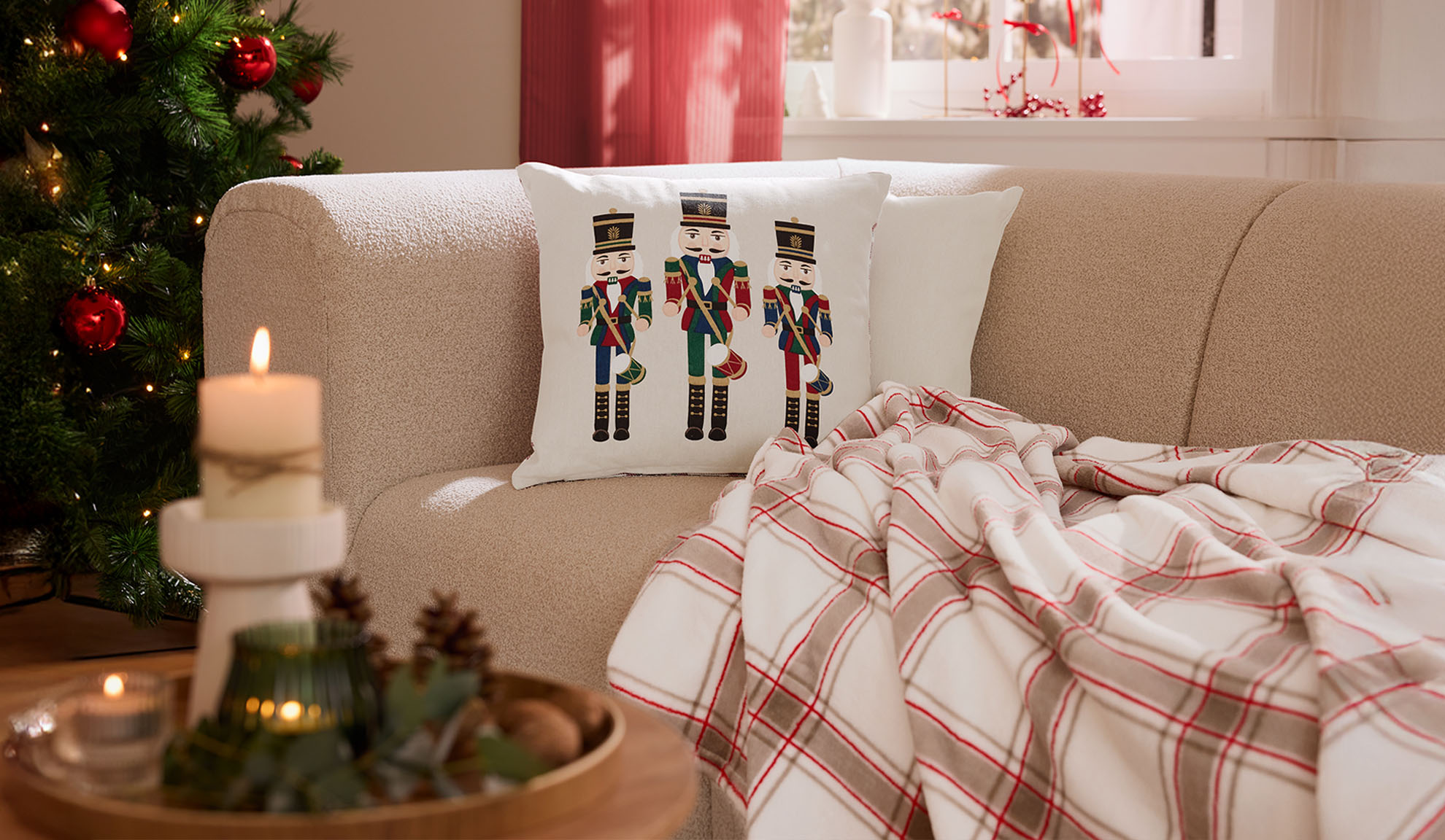 Коледна всекидневна с диван, възглавници с лешникотрошачки, карирано одеяло и свещи.