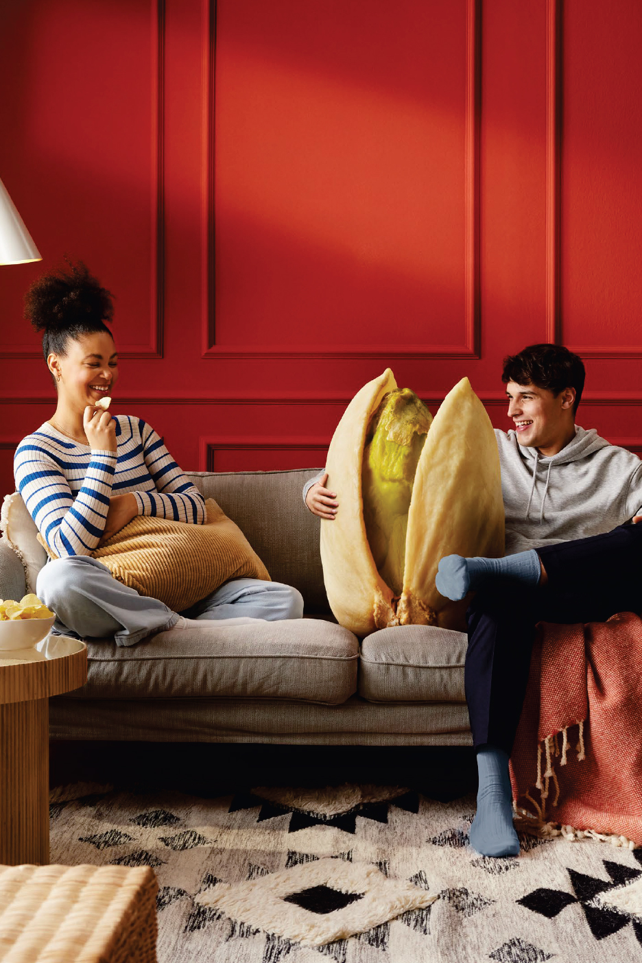 Мъж и жена на диван с гигантски шамфъстък, гледащи телевизия.